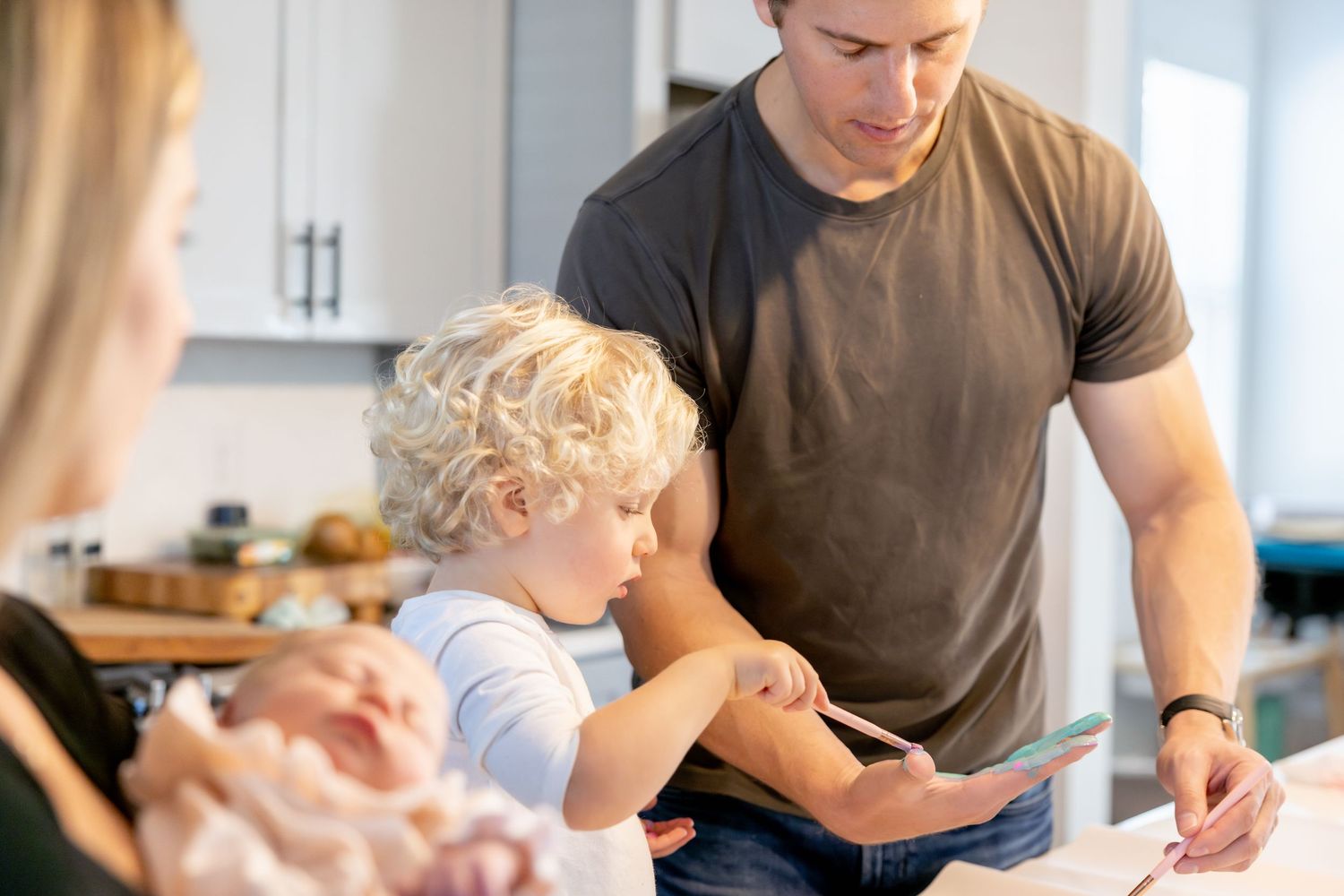 A child and adult engage in creative art activities together at a table in a bright modern kitchen.