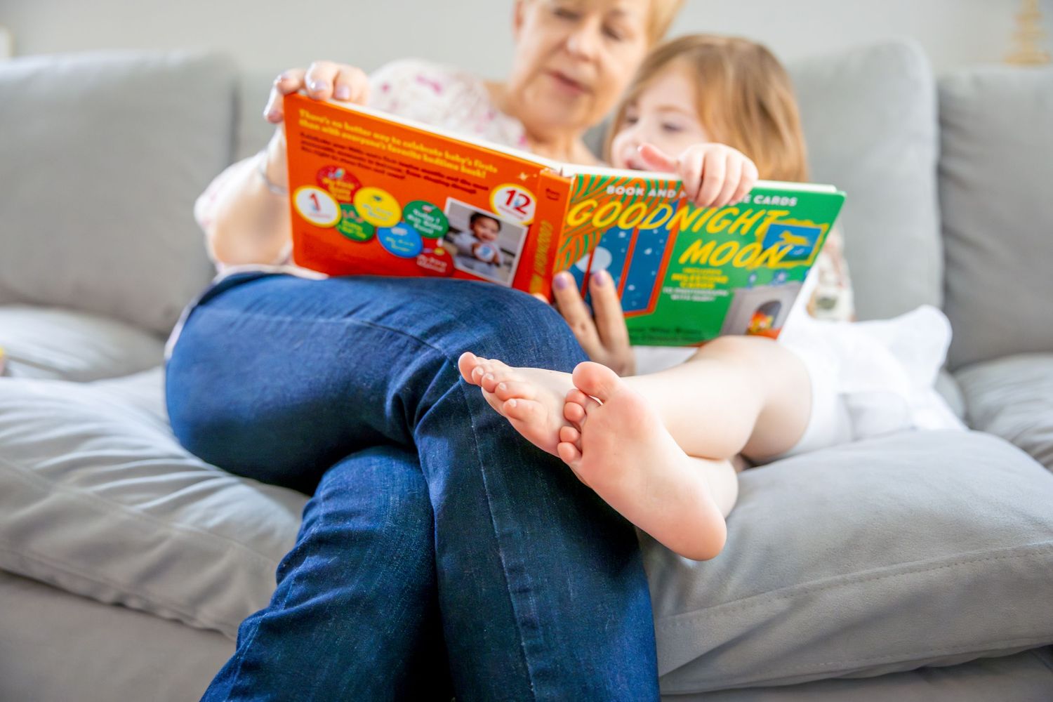 Adult and child reading a colorful storybook together while relaxing on a gray couch.
