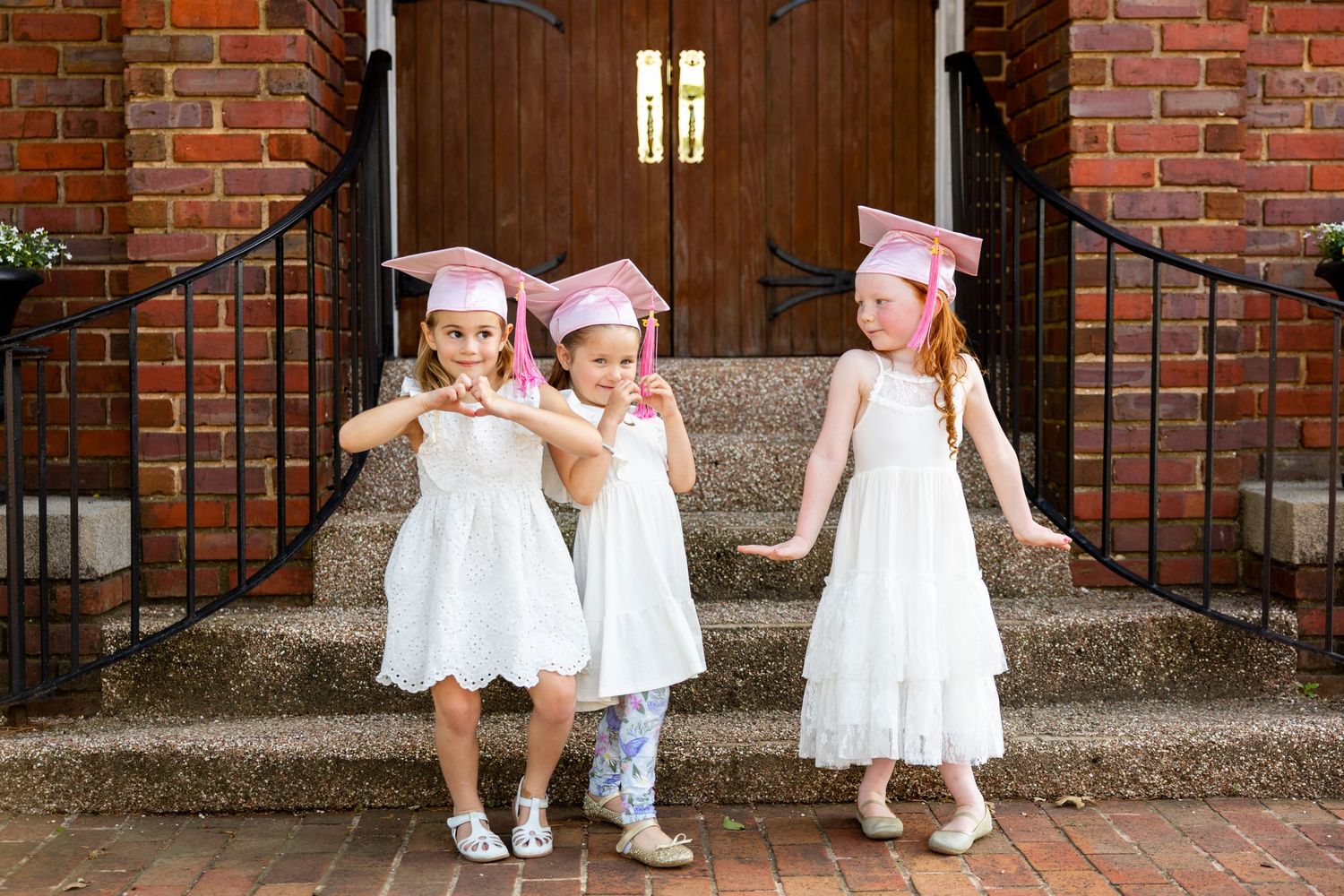Children in preschool graduation caps and white outfits playing together on church steps.