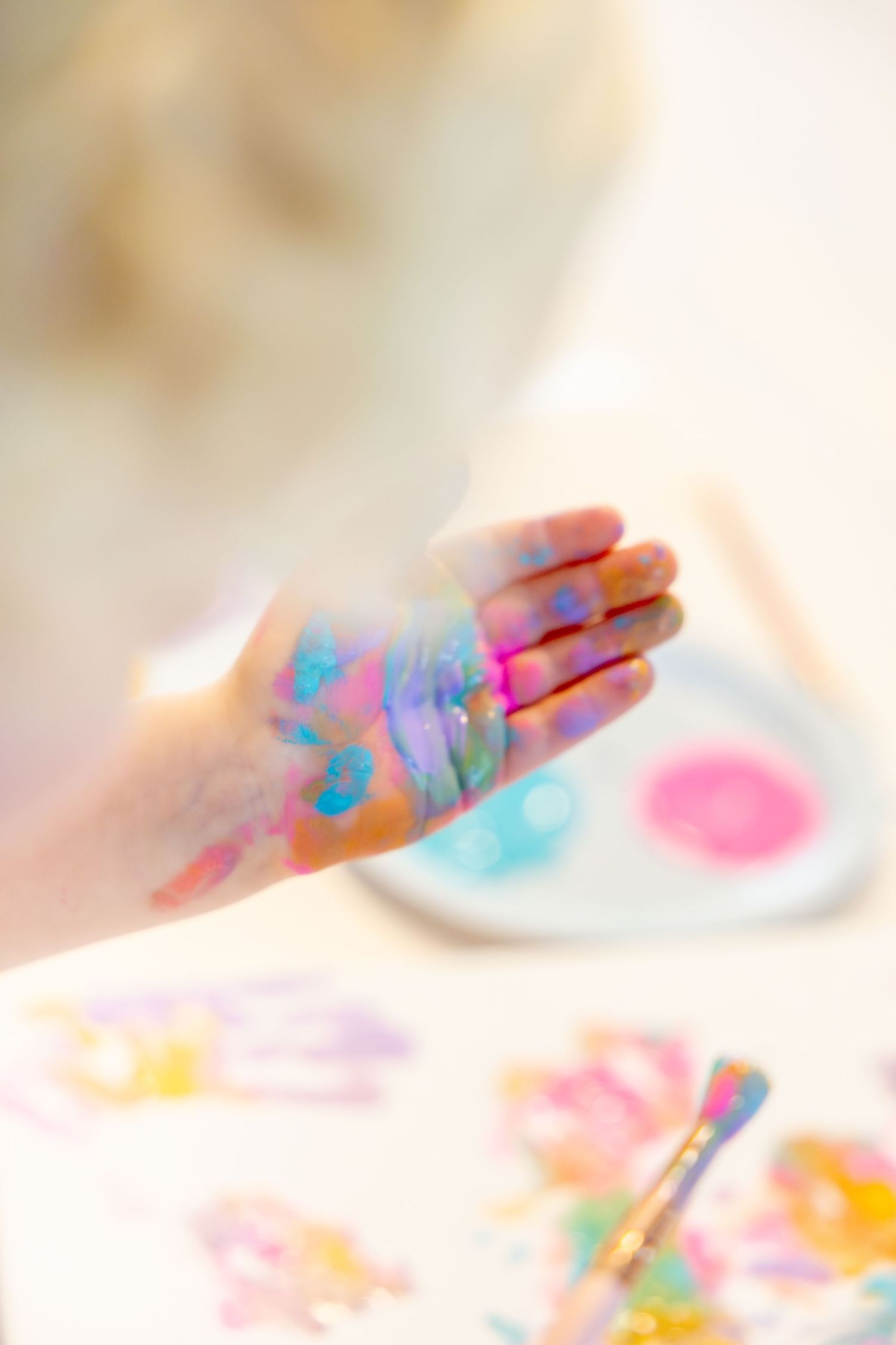 Hand covered in vibrant finger paint colors showing through a soft focus lens.