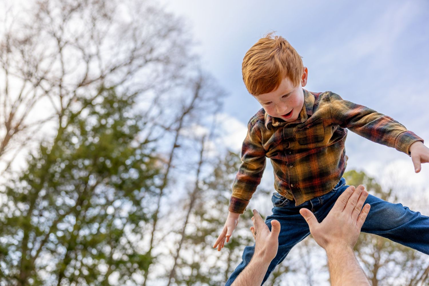 Child being lifted high in the air against a bright blue sky and trees.