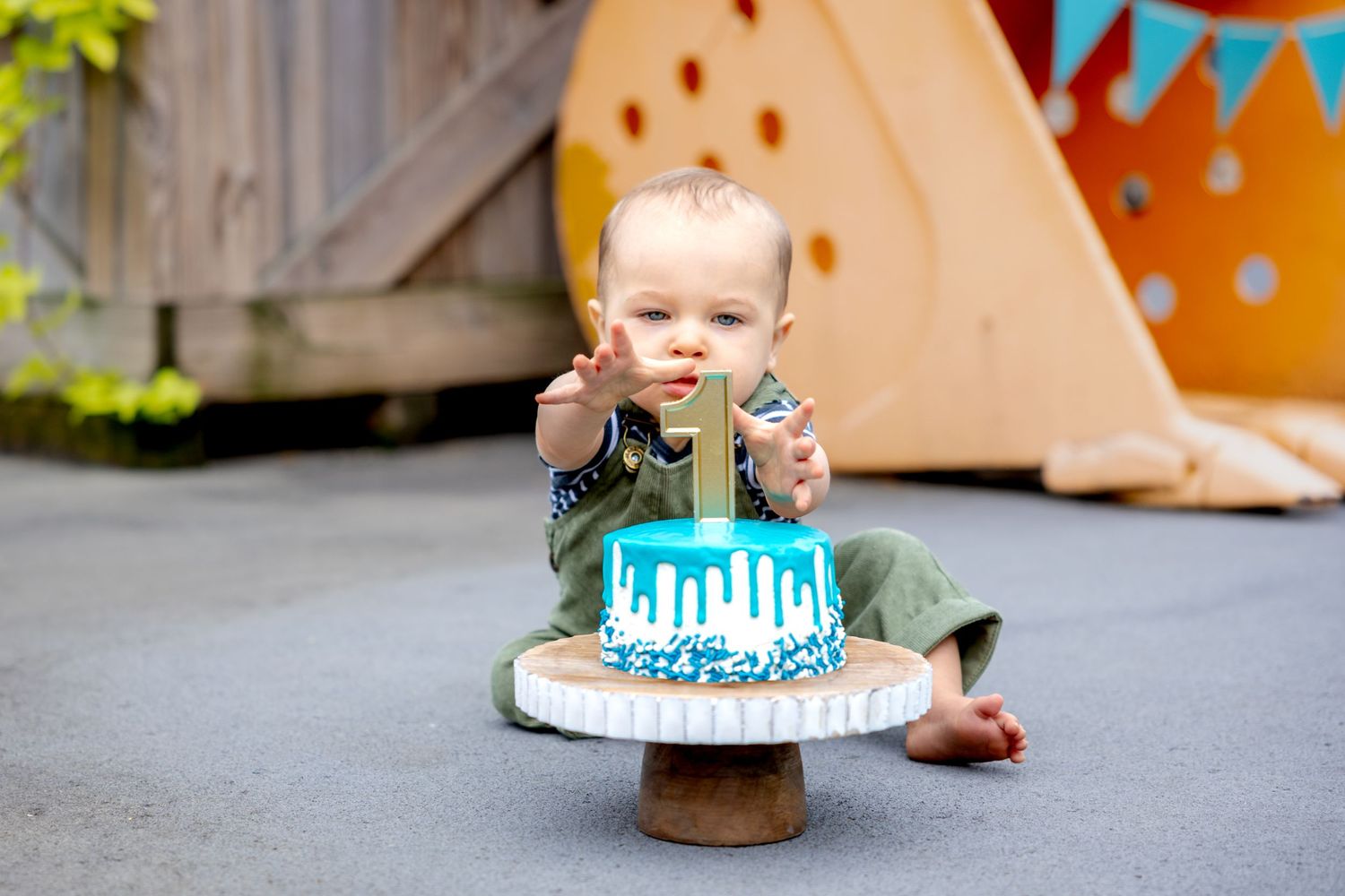 A joyful cake smash session with a turquoise drip cake and festive decorations located at Camp North End in Charlotte, NC.