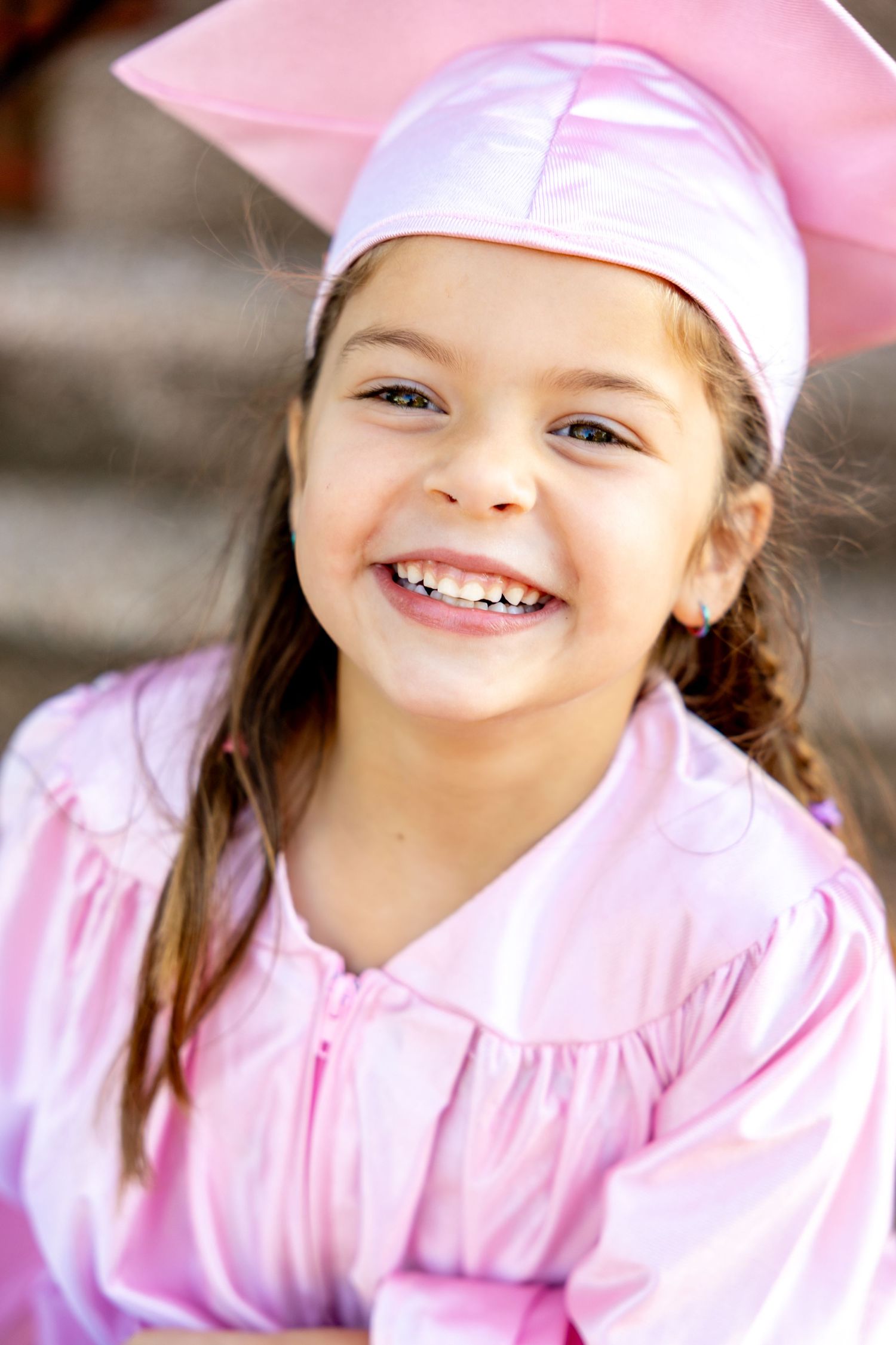 Joyful portrait of preschool graduate in pink cap and gown.