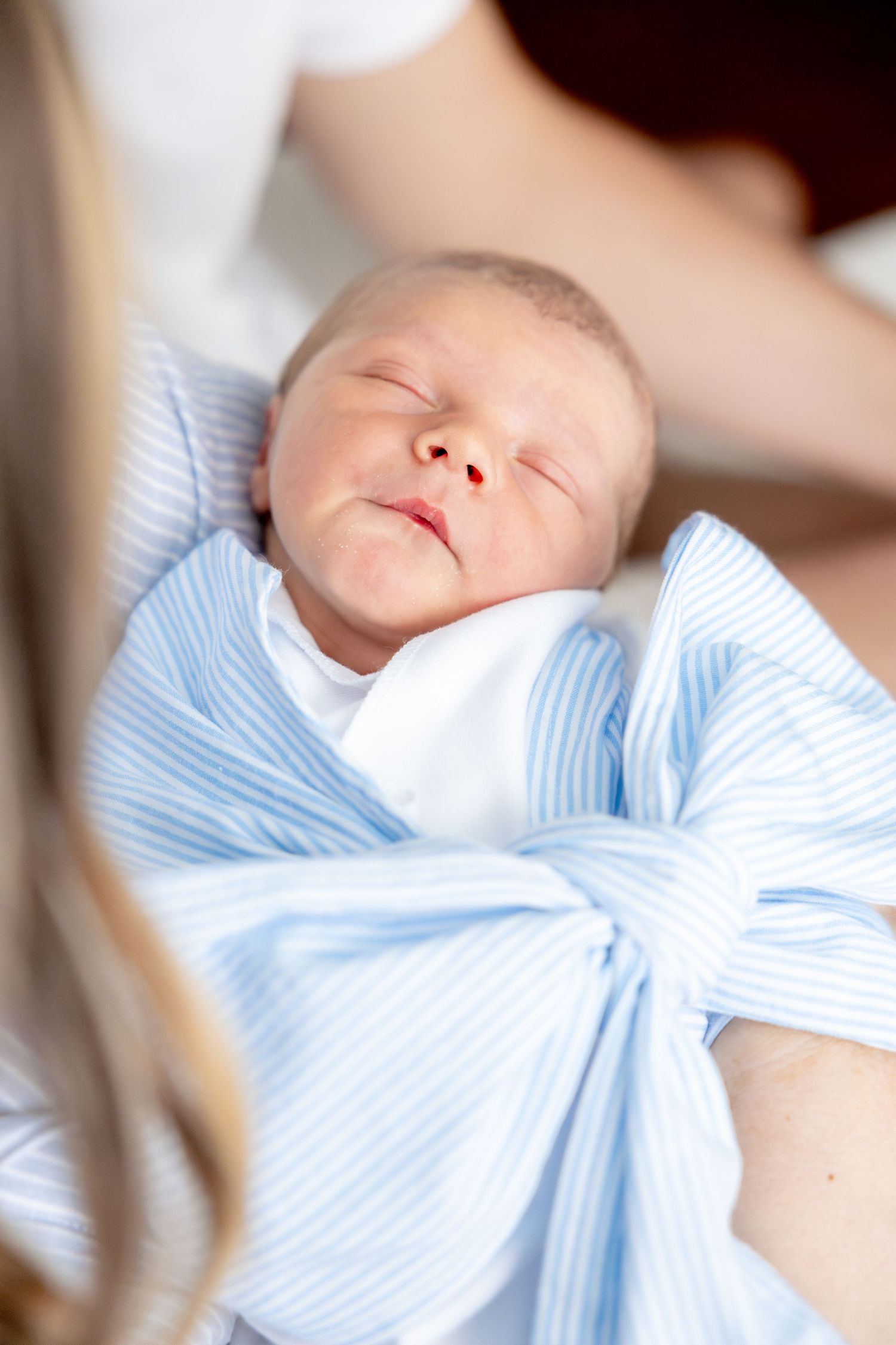 Peaceful sleeping newborn baby swaddled in light blue and white striped blanket.