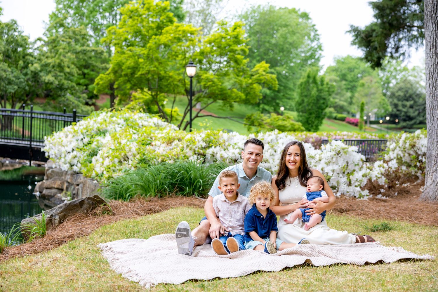 Family enjoys a picturesque outdoor gathering on a blanket near a pond surrounded by lush greenery.