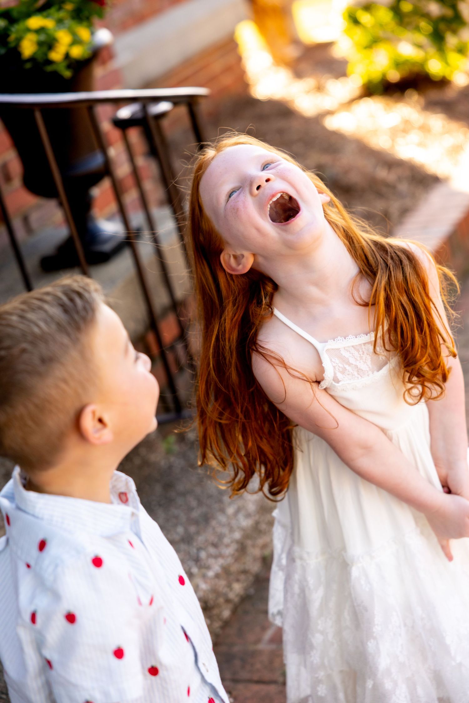 Joyful children laughing and playing against a brick wall in natural sunlight.