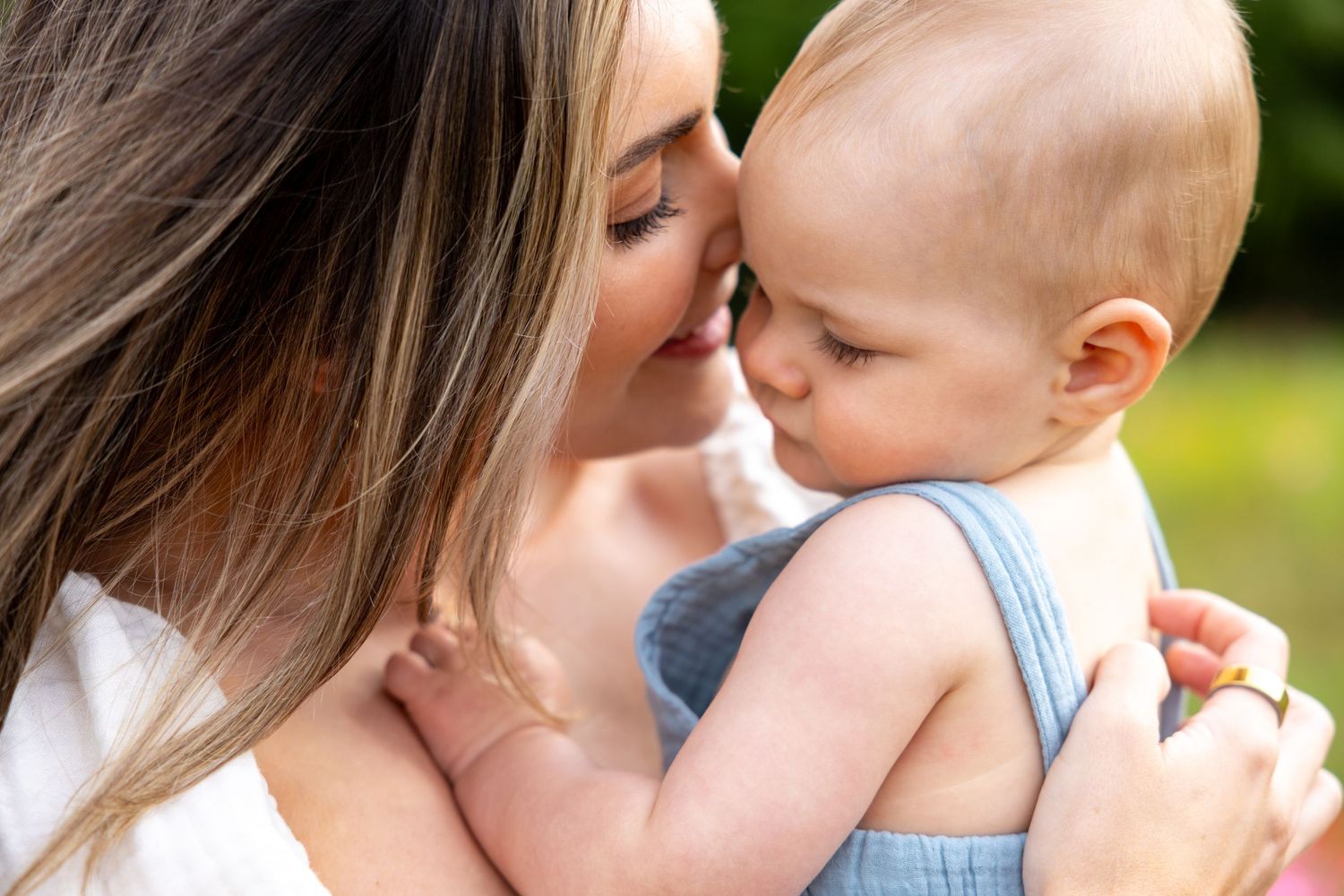 Tender moment between mother and baby against blurred green background at Blue Hill Garden in Monroe, NC.