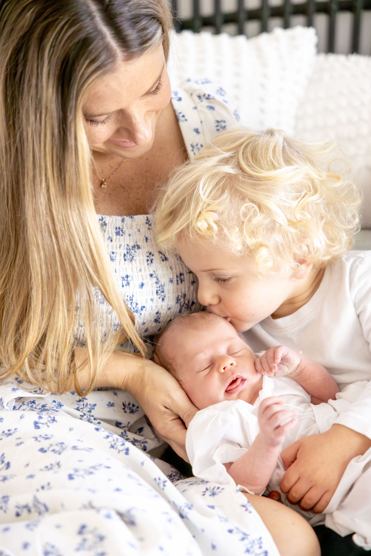 Tender family moment captured in soft natural light on white bedding.