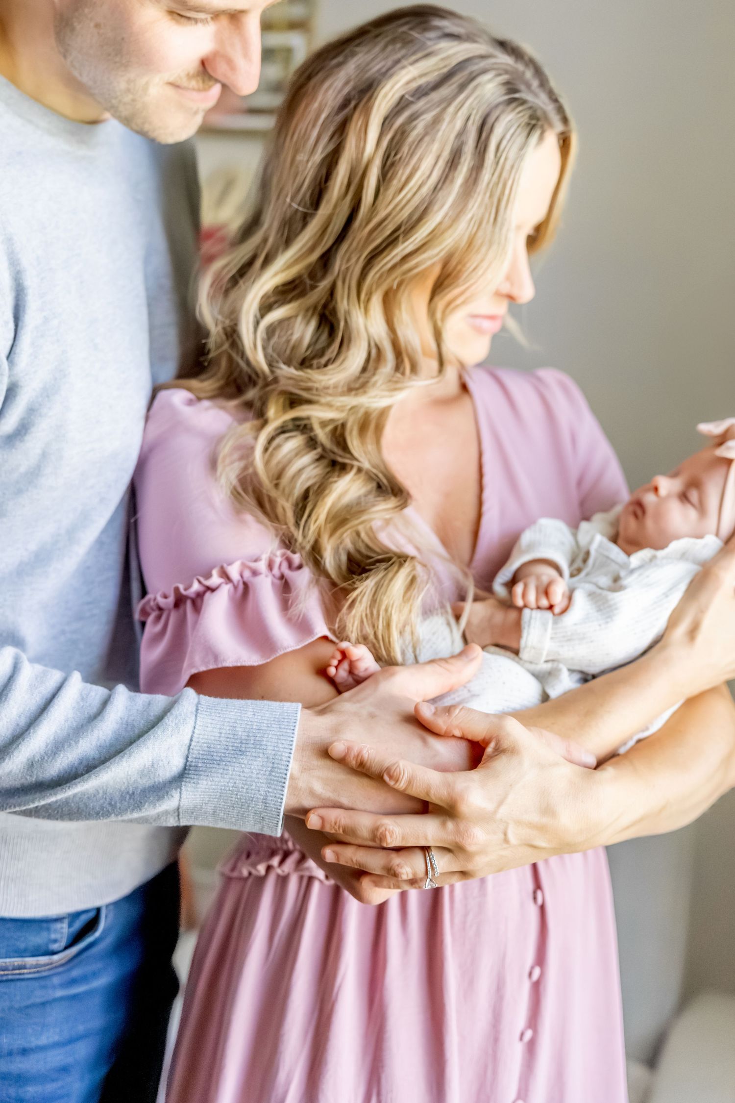 Couple in pink dress and grey sweater tenderly holding small baby.