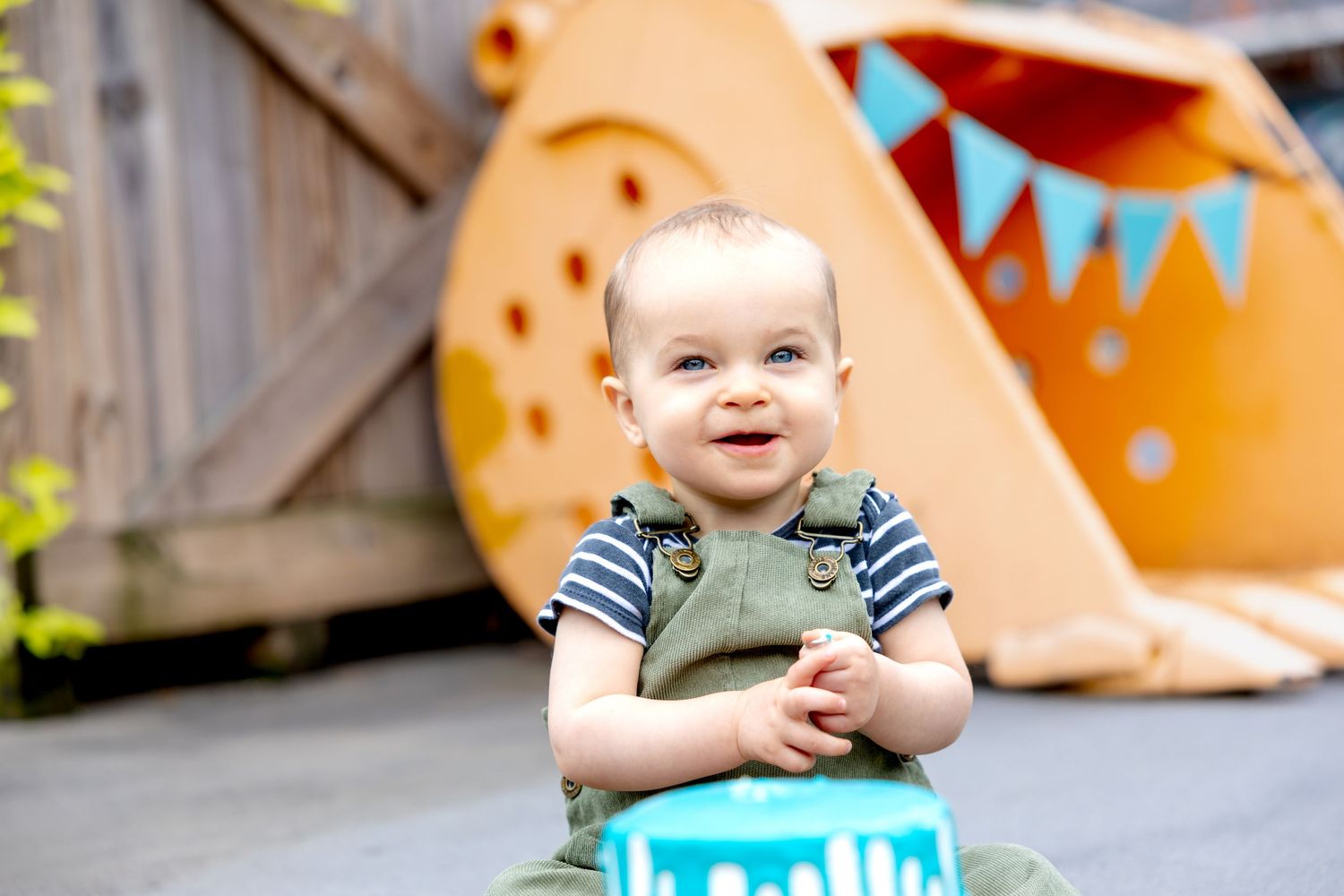 A first birthday cake smash session of toddler with a turquoise drip cake and festive decorations at Camp North End in Charlotte, NC.