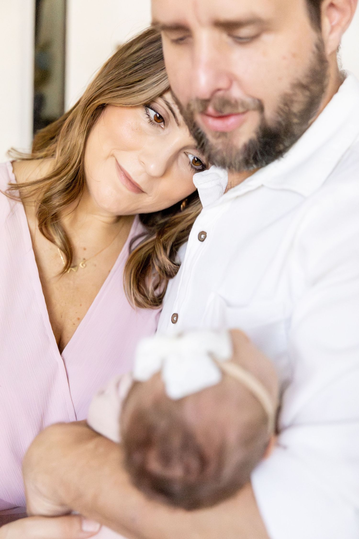 Family shares tender moment together while holding newborn baby in soft natural light.