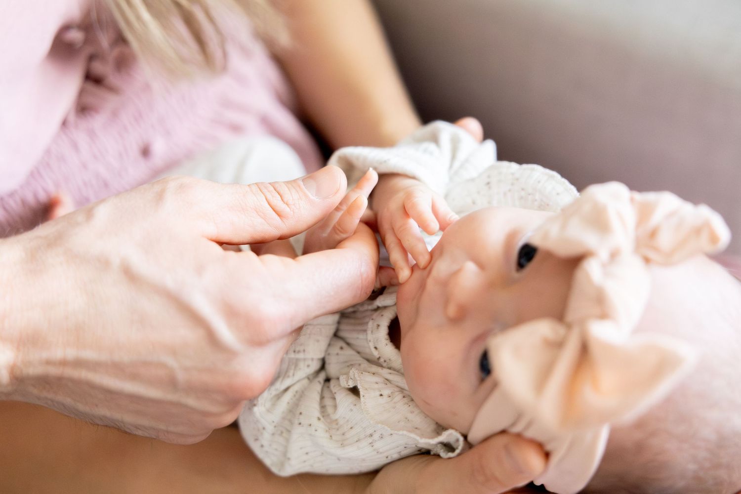 Baby in white ruffled outfit being cradled by caring hands.