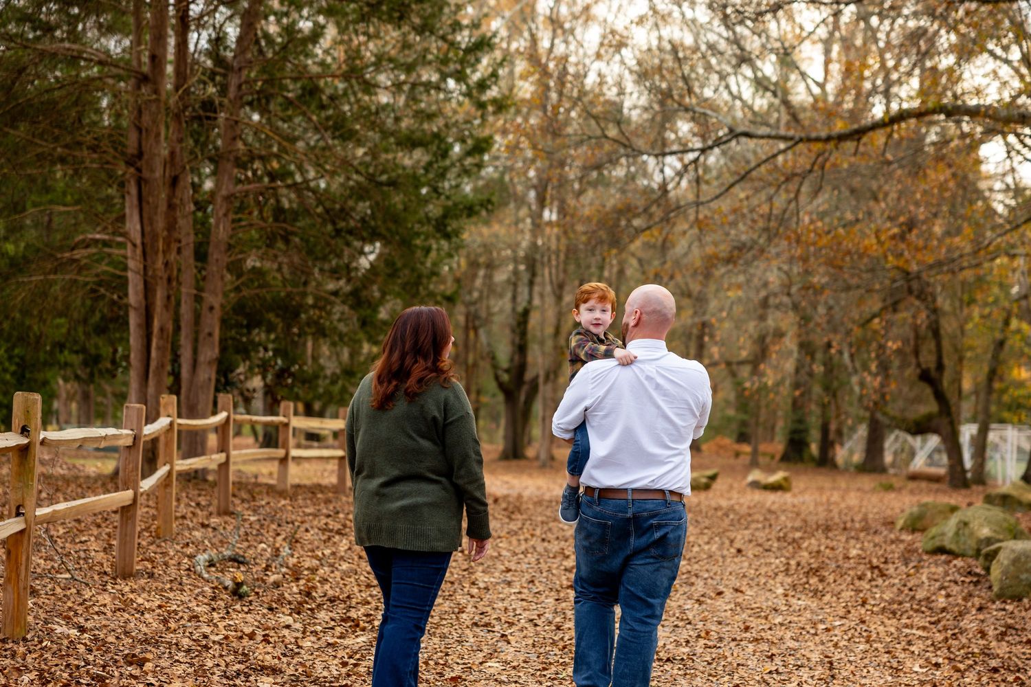 Family walking together on leaf-covered trail in autumn woods.