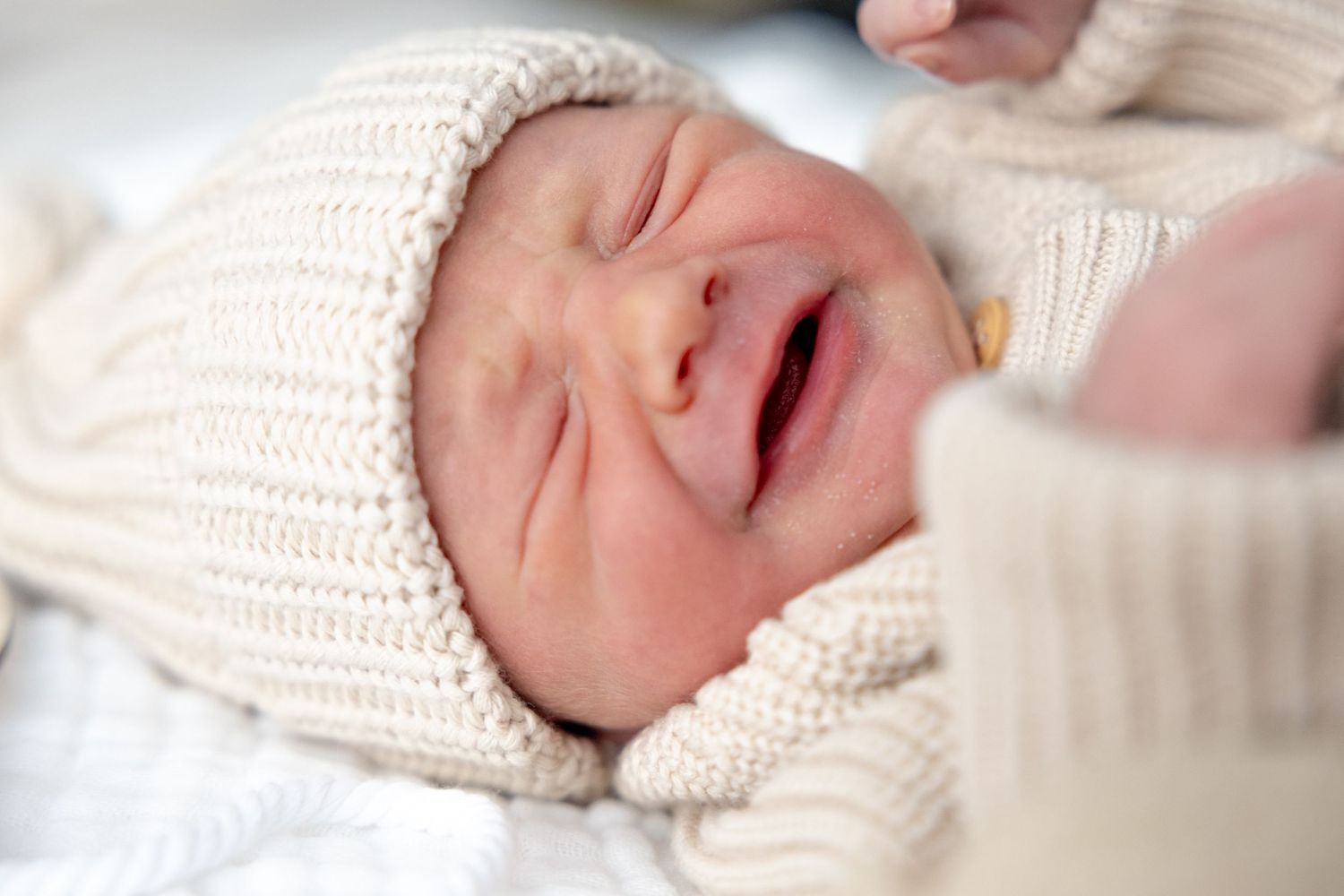Newborn baby in knit sweater crying with expressive face.