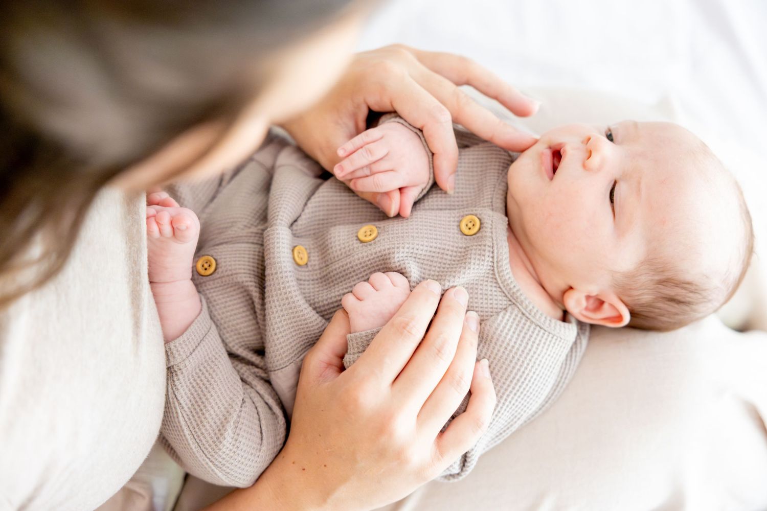 Close up of hands gently holding infant wearing gray onesie.