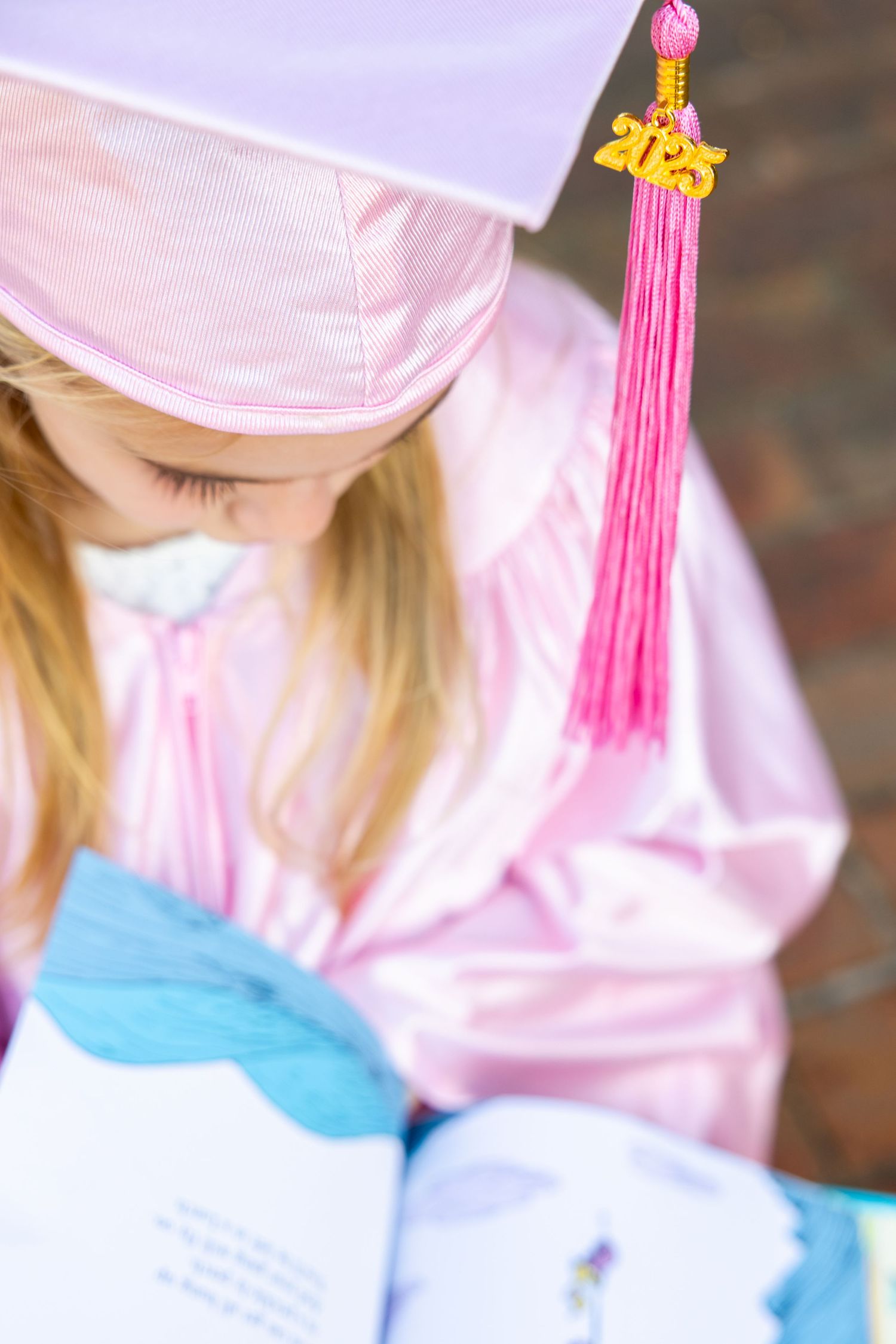 Detail shots of pink preschool graduation cap with tassel and blue diploma holder.