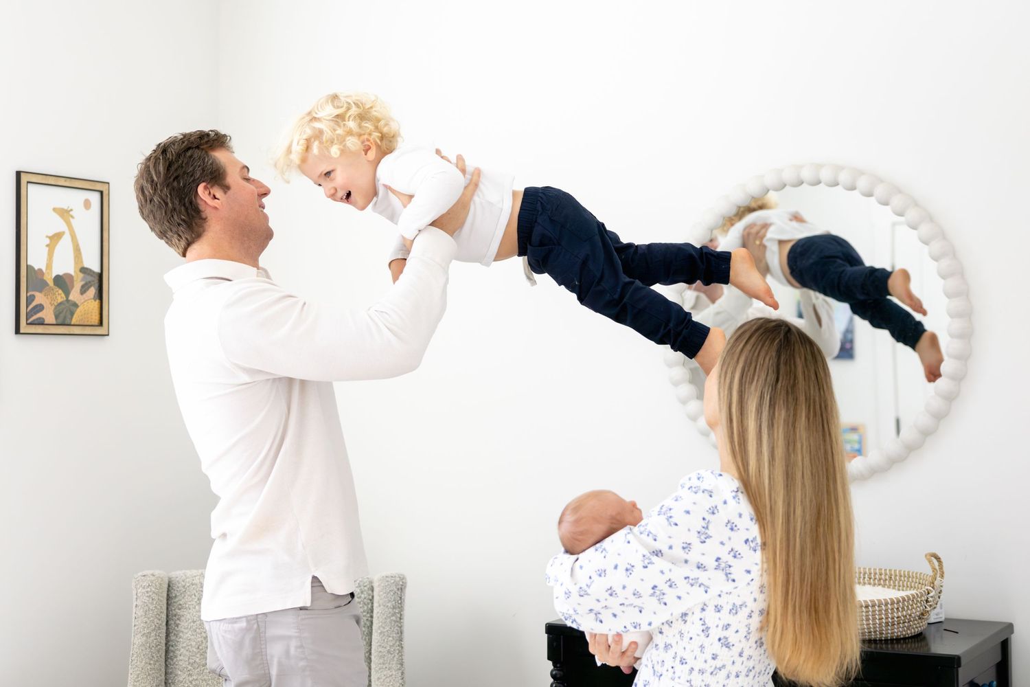 Playful family moment captured in front of circular mirror in nursery.