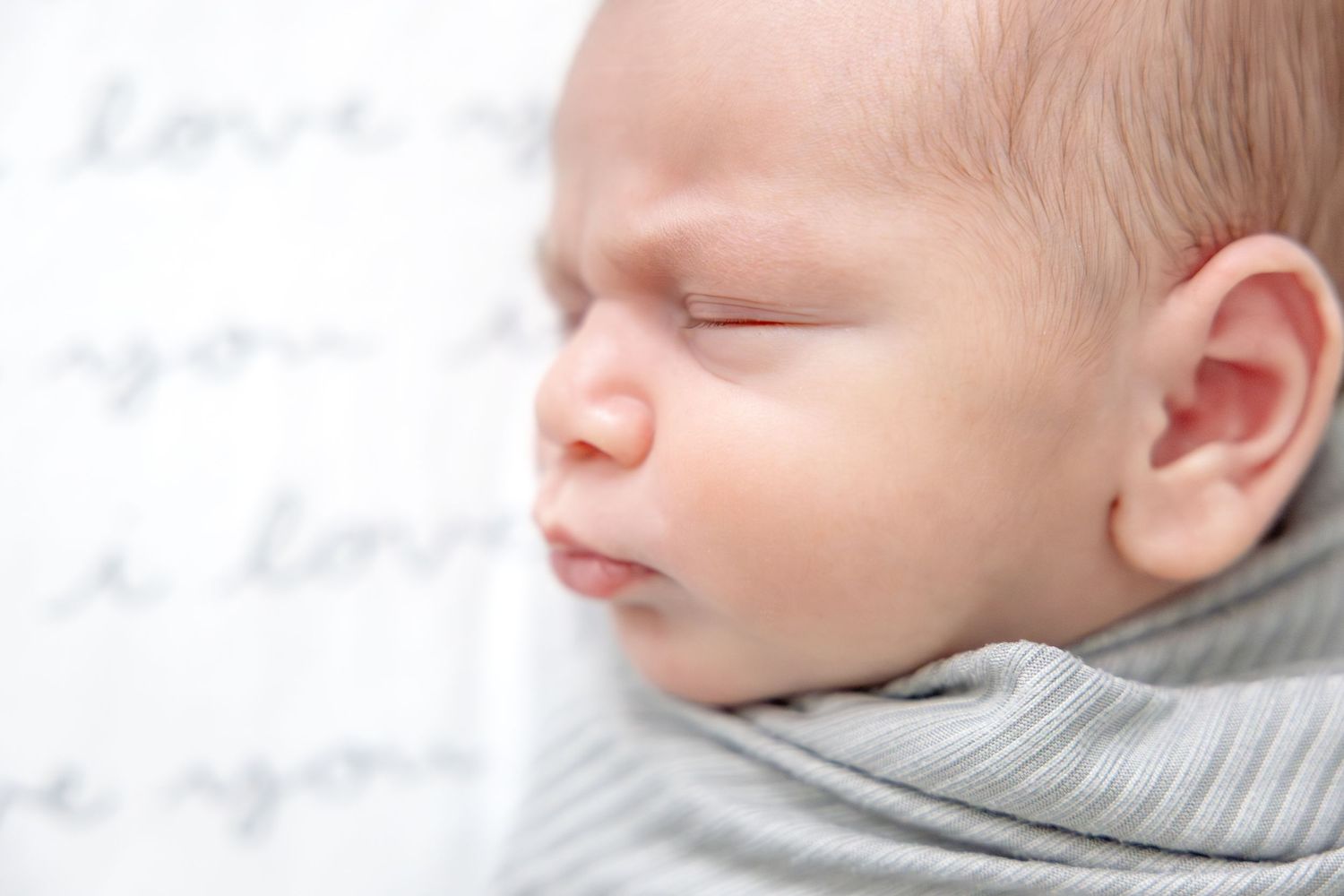 Close-up portrait of newborn sleeping peacefully on white bedding.