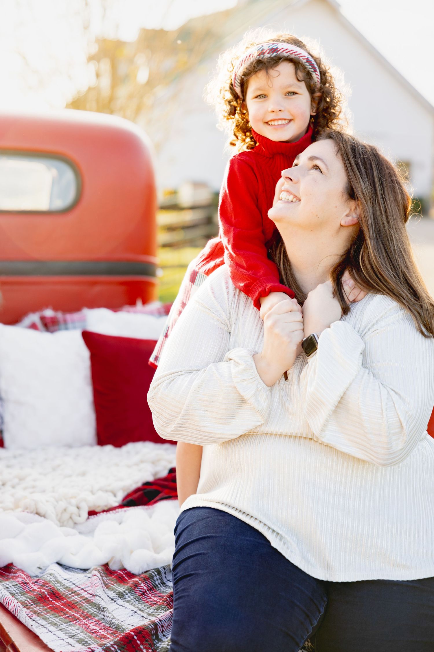 Mother and child share playful moments on plaid blanket with red truck in background.
