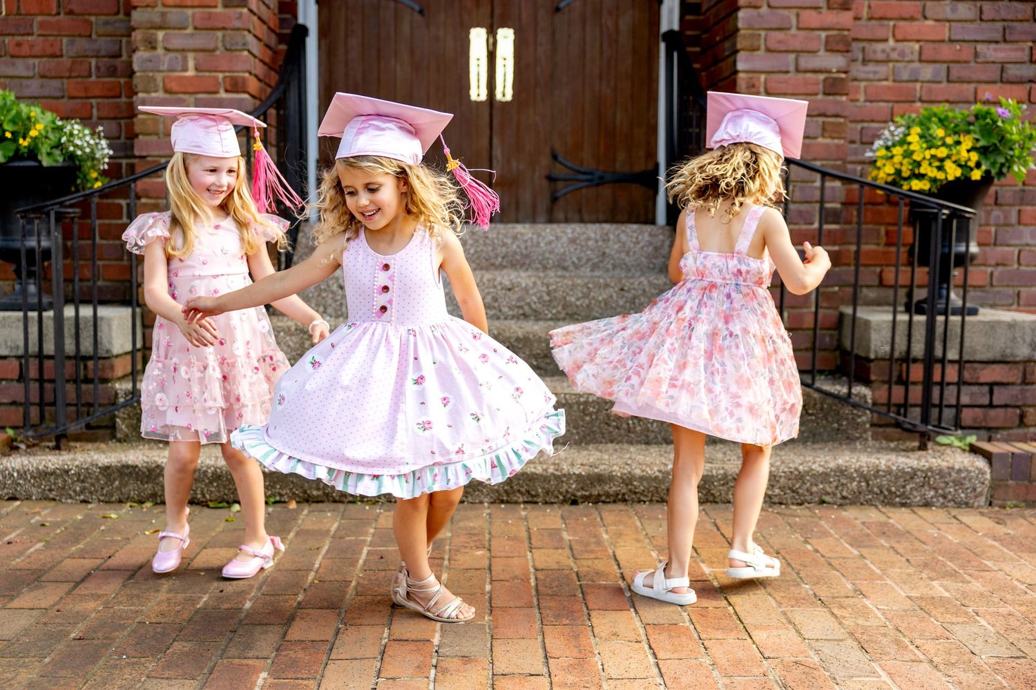 A sequence of twirling movements in pink dresses and pink preschool graduation caps on a brick patio.
