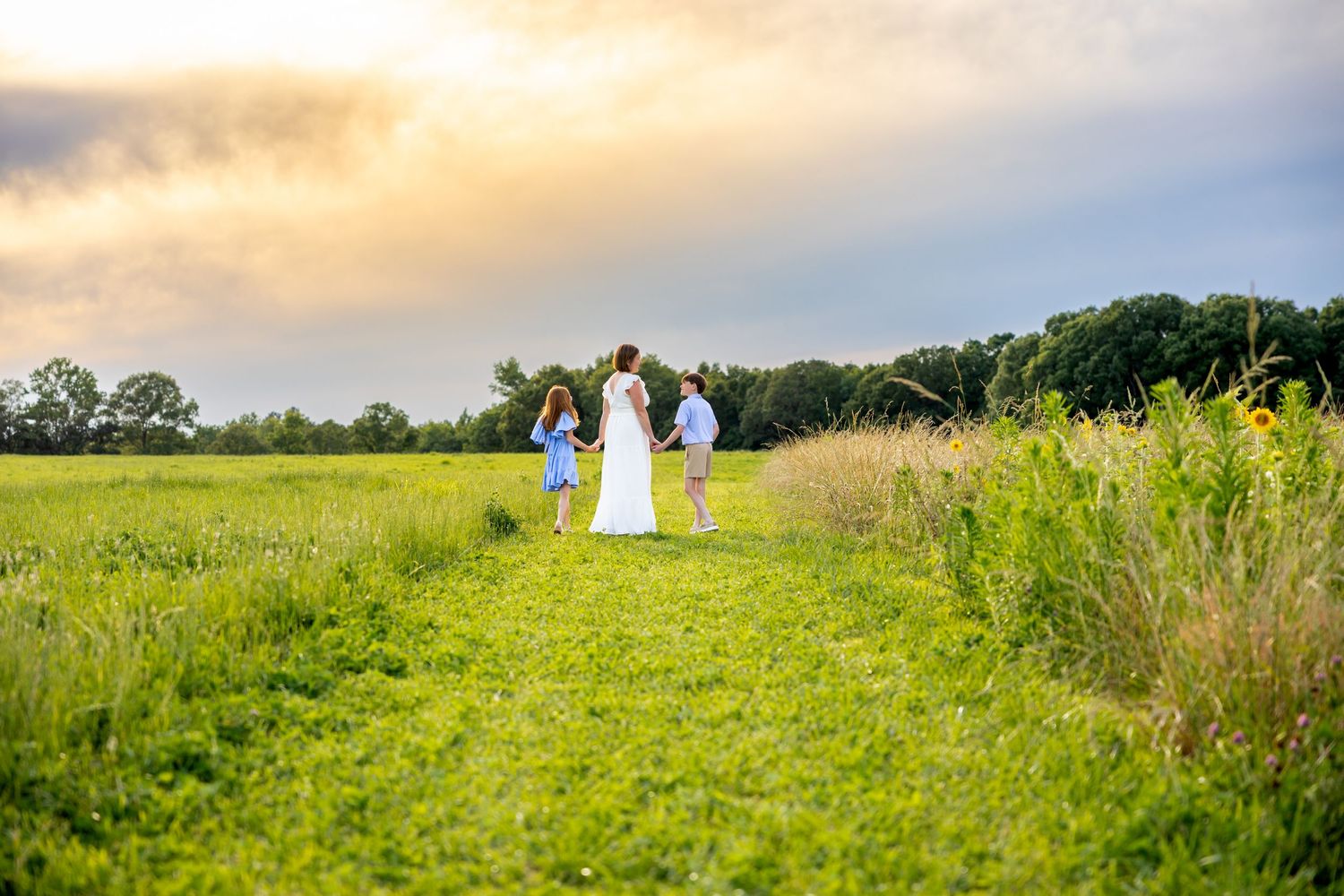 Distant figures walking through a green meadow path at sunset at Blue Hill Garden in Monroe, NC.