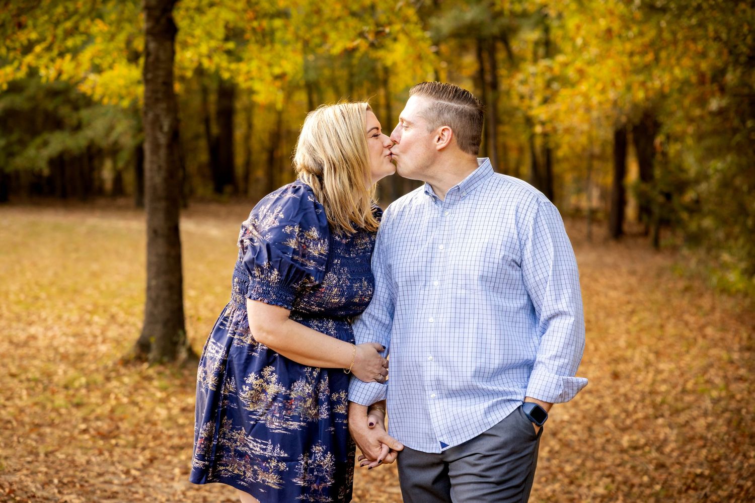 Couple sharing an intimate moment in a forest with golden fall foliage.