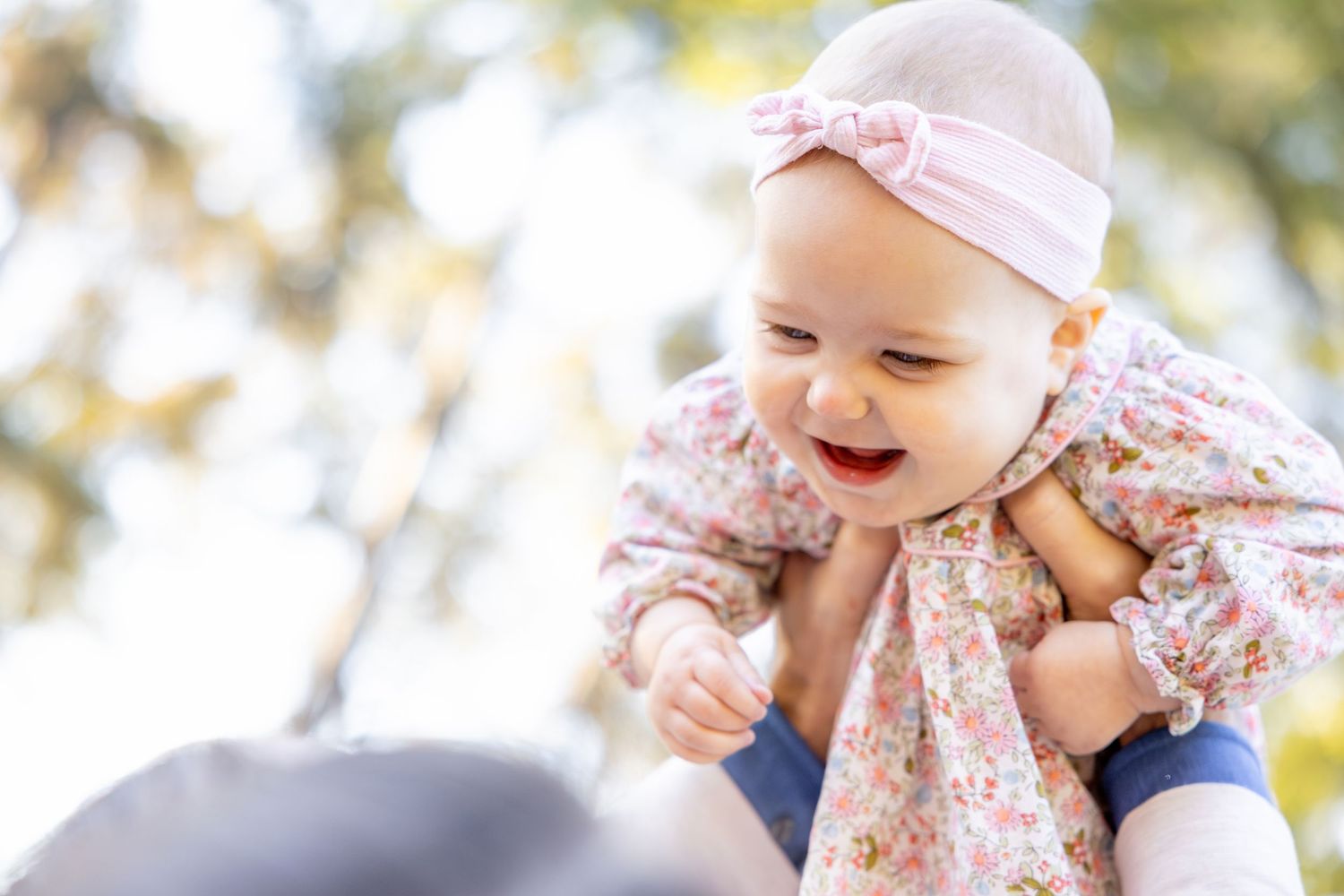 Infant in pink floral outfit playing outdoors in golden sunlight.