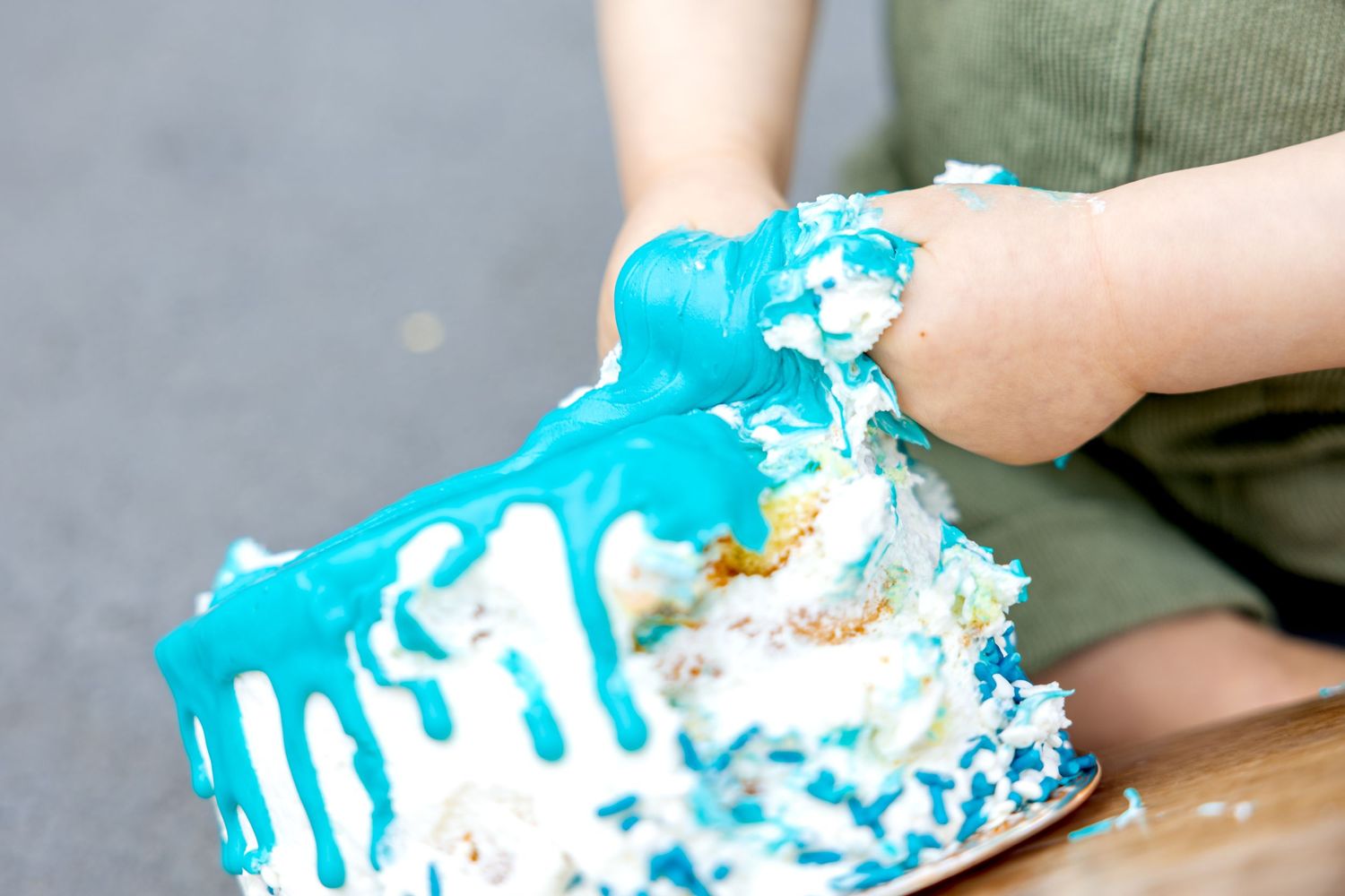 Small hands covered in bright turquoise frosting from smashing into a birthday cake during a sweet cake smash session.