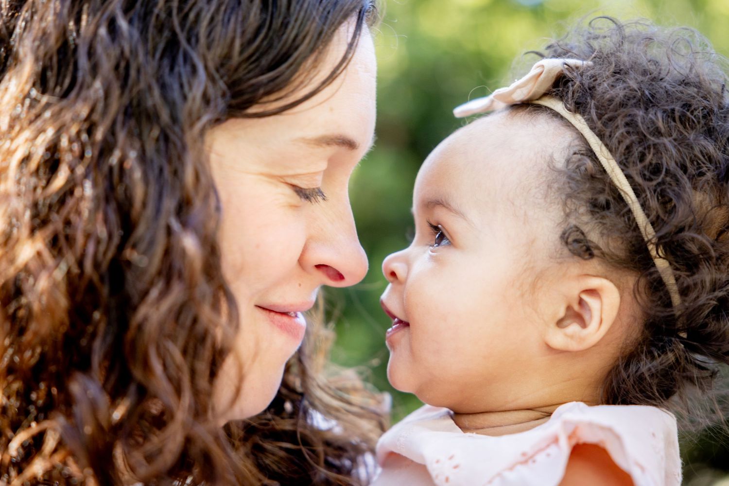 Close-up profile view of tender moment between adult and baby in outdoor setting.