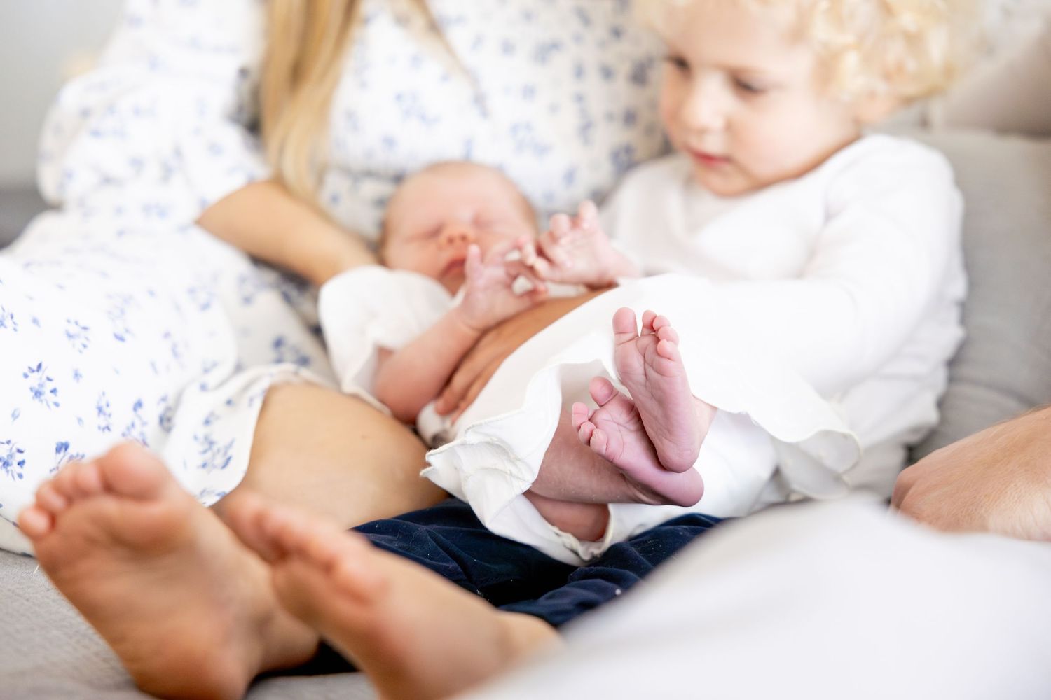 Intimate family moment captured on white bedding with blue floral pattern.