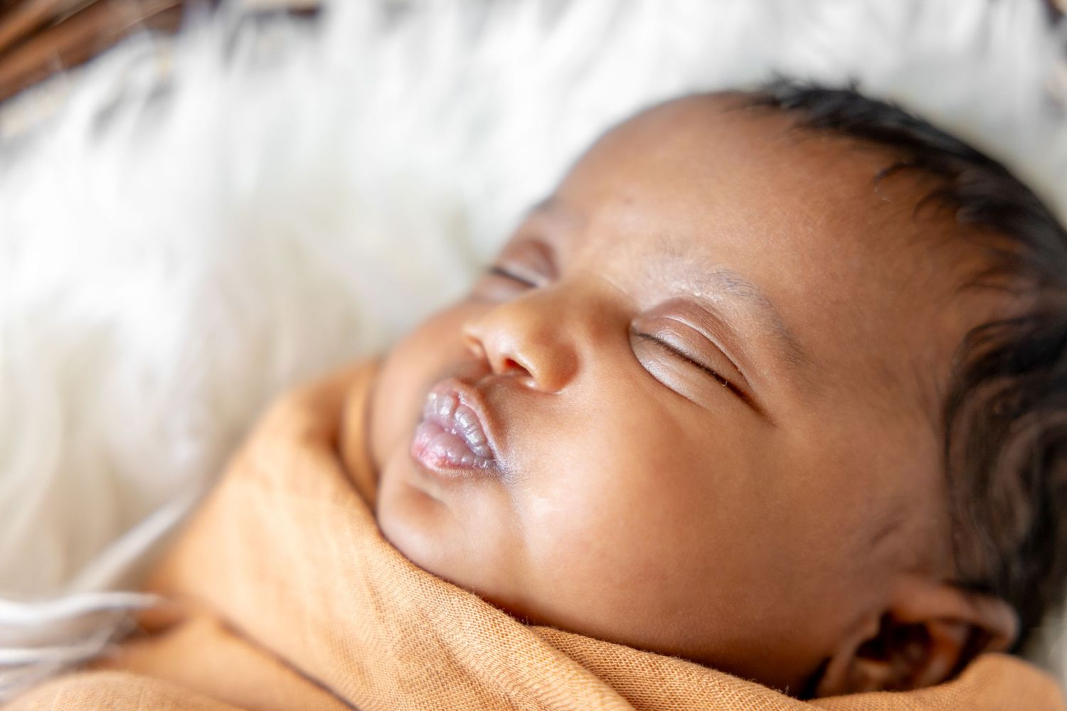 Peaceful sleeping newborn baby wrapped in orange blanket on white fur background.