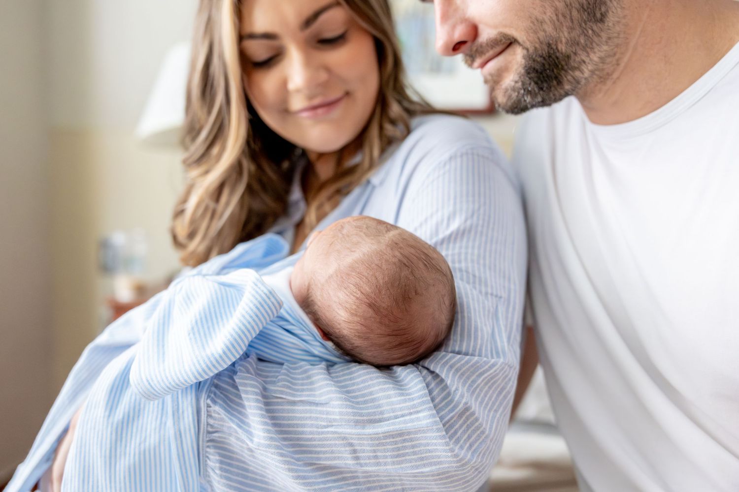 Parents admiring their sleeping newborn wrapped in light blue swaddle.