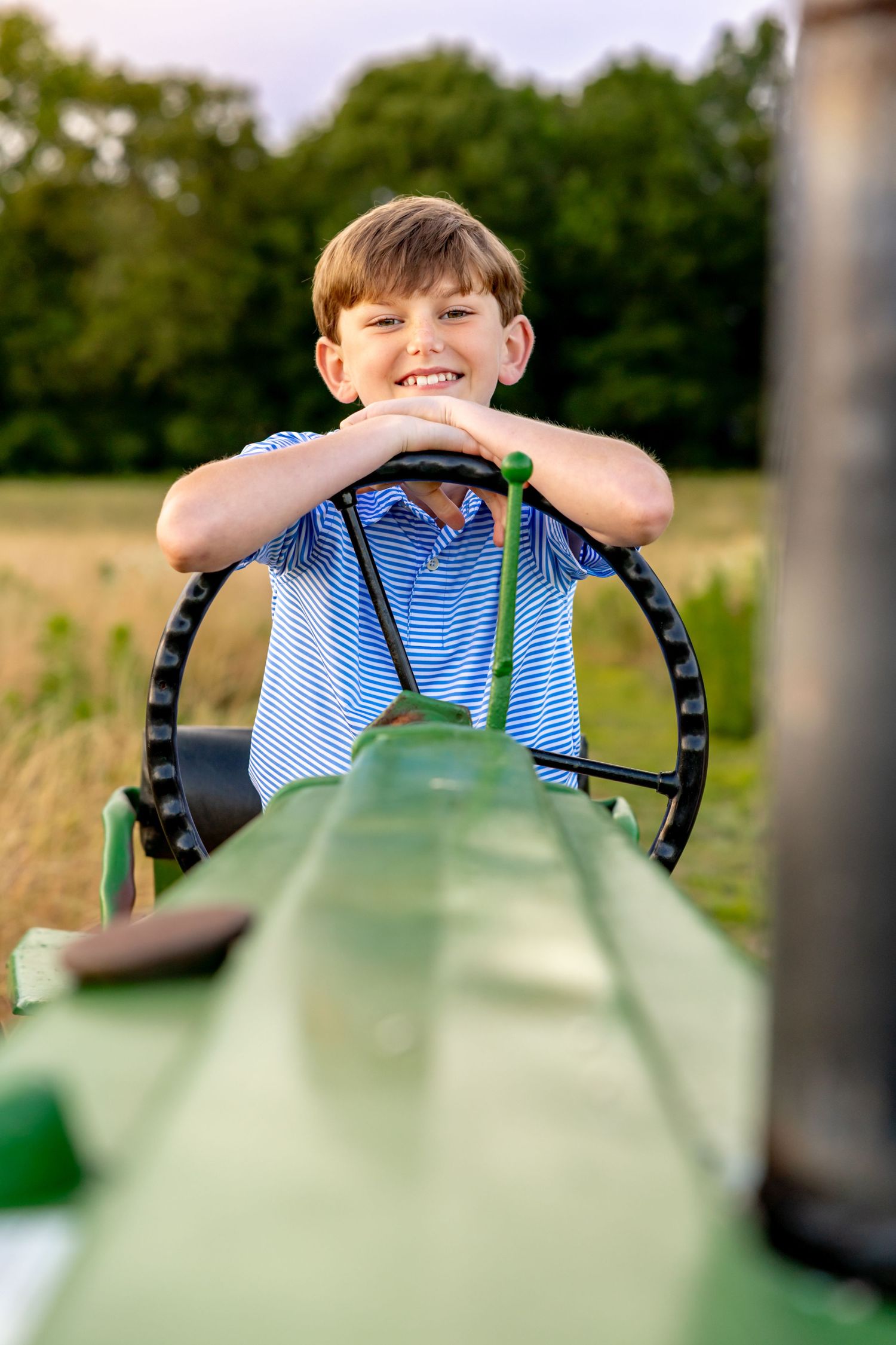Child sitting at the steering wheel of a green tractor during a fun outdoor photoshoot at Blue Hill Garden in Monroe, NC.
