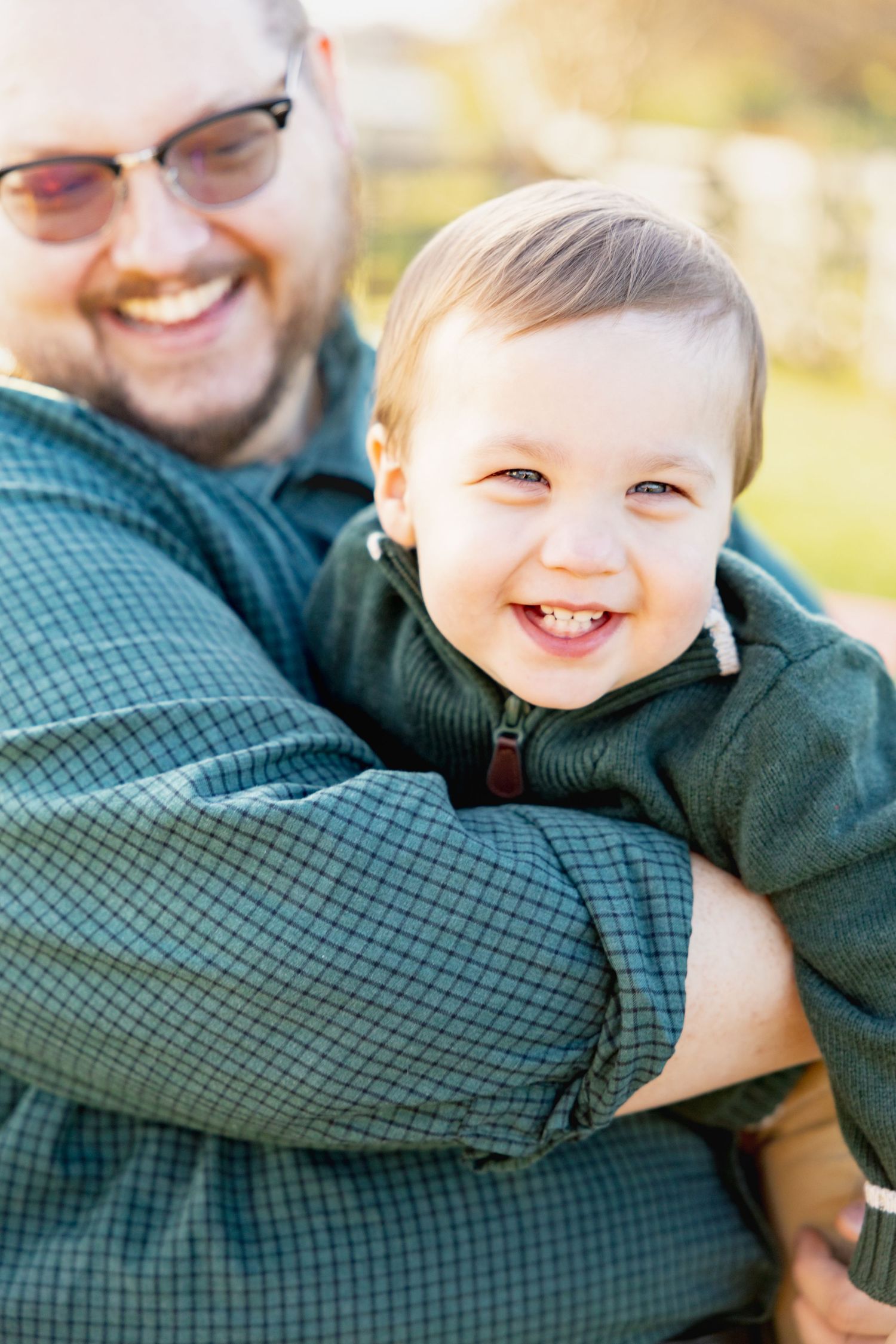Close up shot of smiling toddler being held outdoors on sunny day.