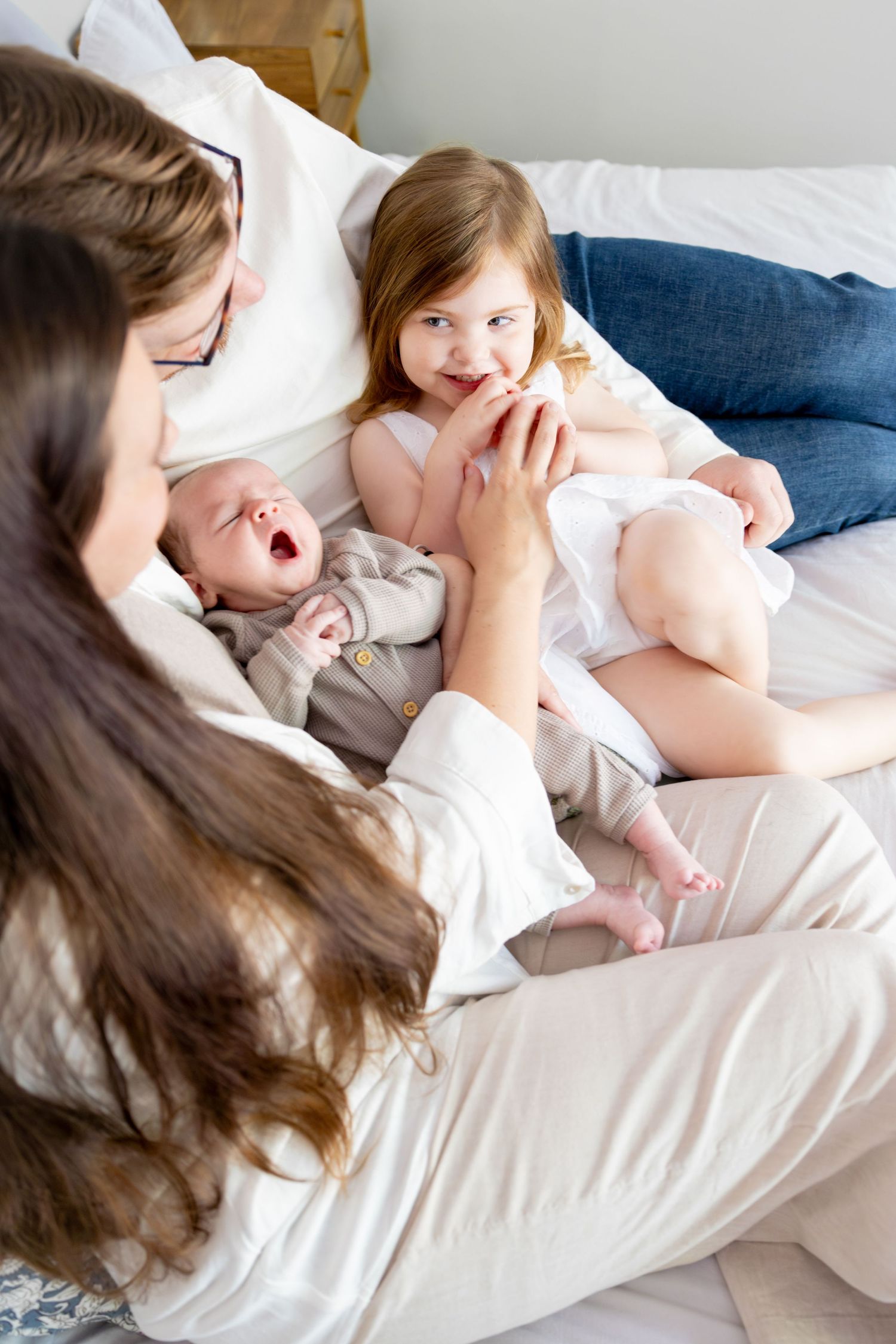 Family bonding moment on white bedding with baby and siblings.
