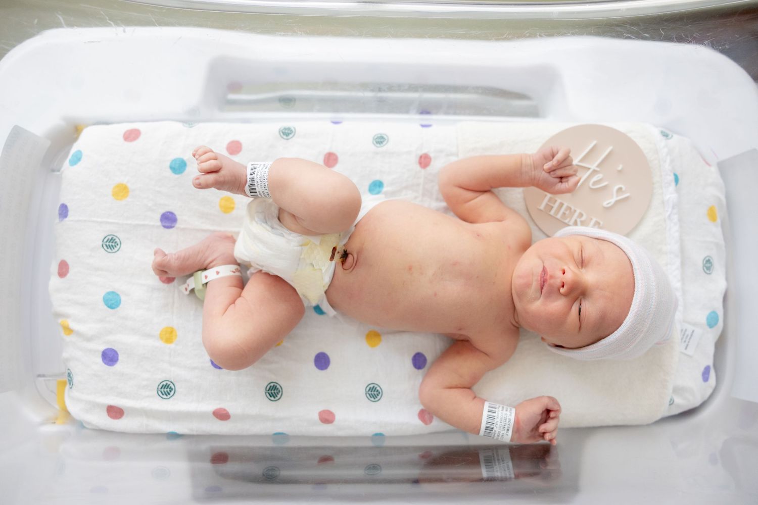 Sleeping newborn on polka dot changing pad during medical examination.