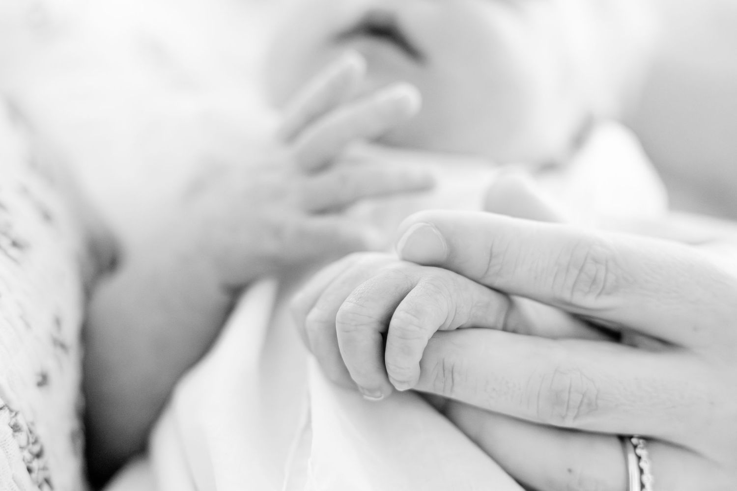 Close-up black and white image of tiny baby hands grasping adult fingers.