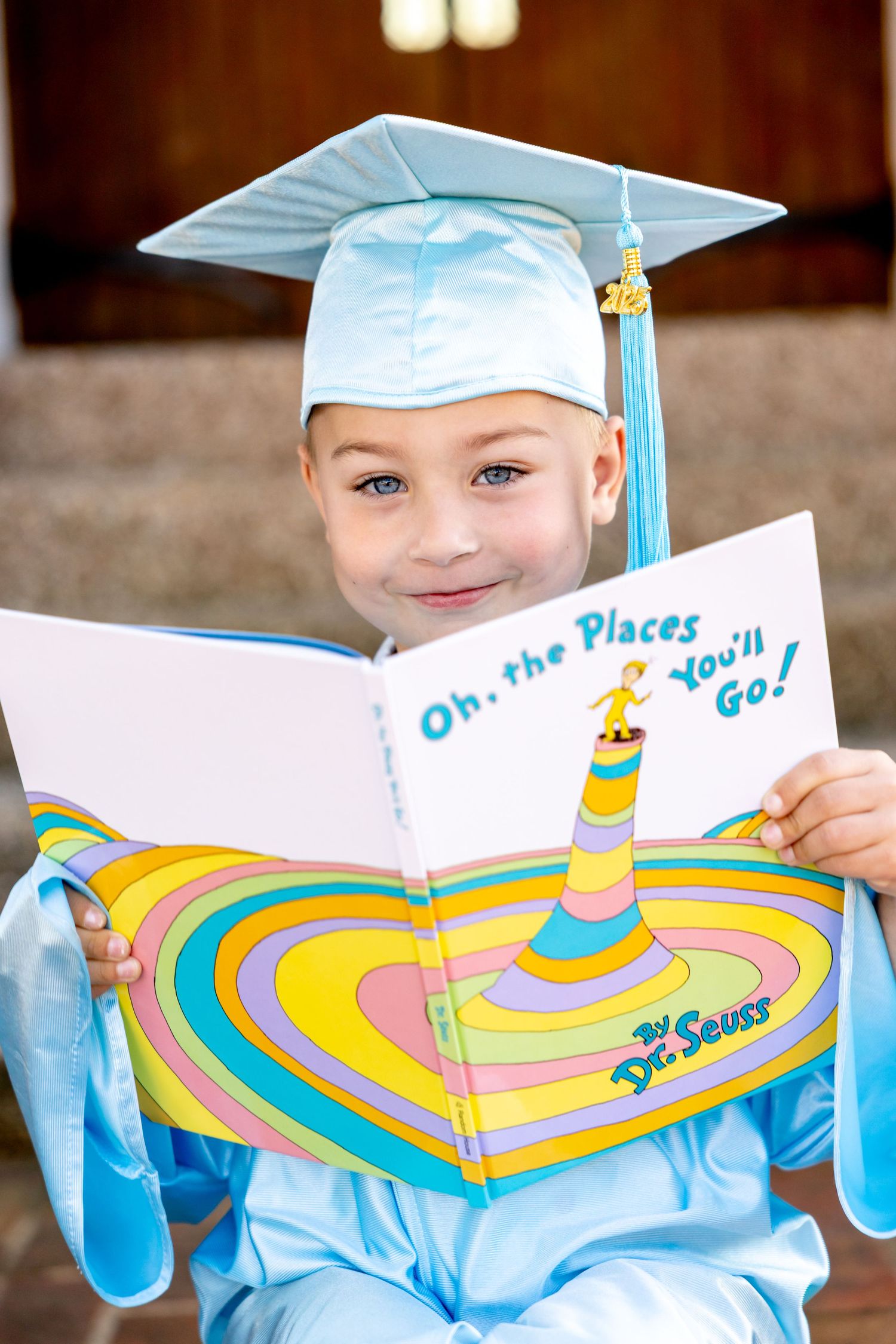 Someone wearing a light blue graduation cap and gown holding a colorful Dr. Seuss book.