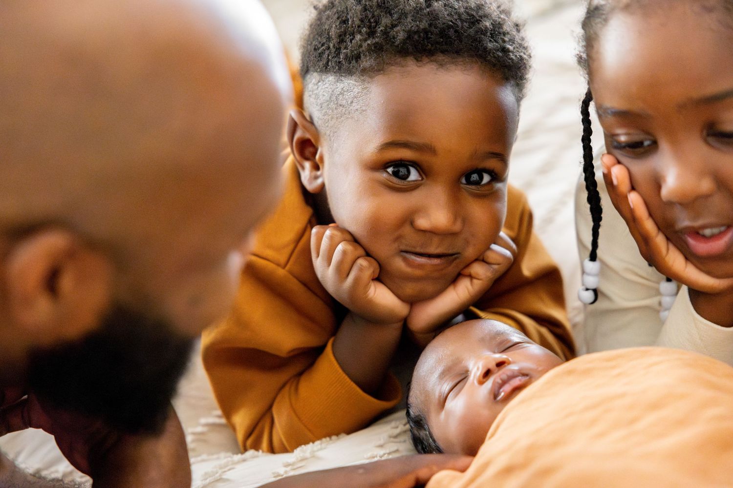 Intimate family moment gathered around sleeping baby on white bedding.