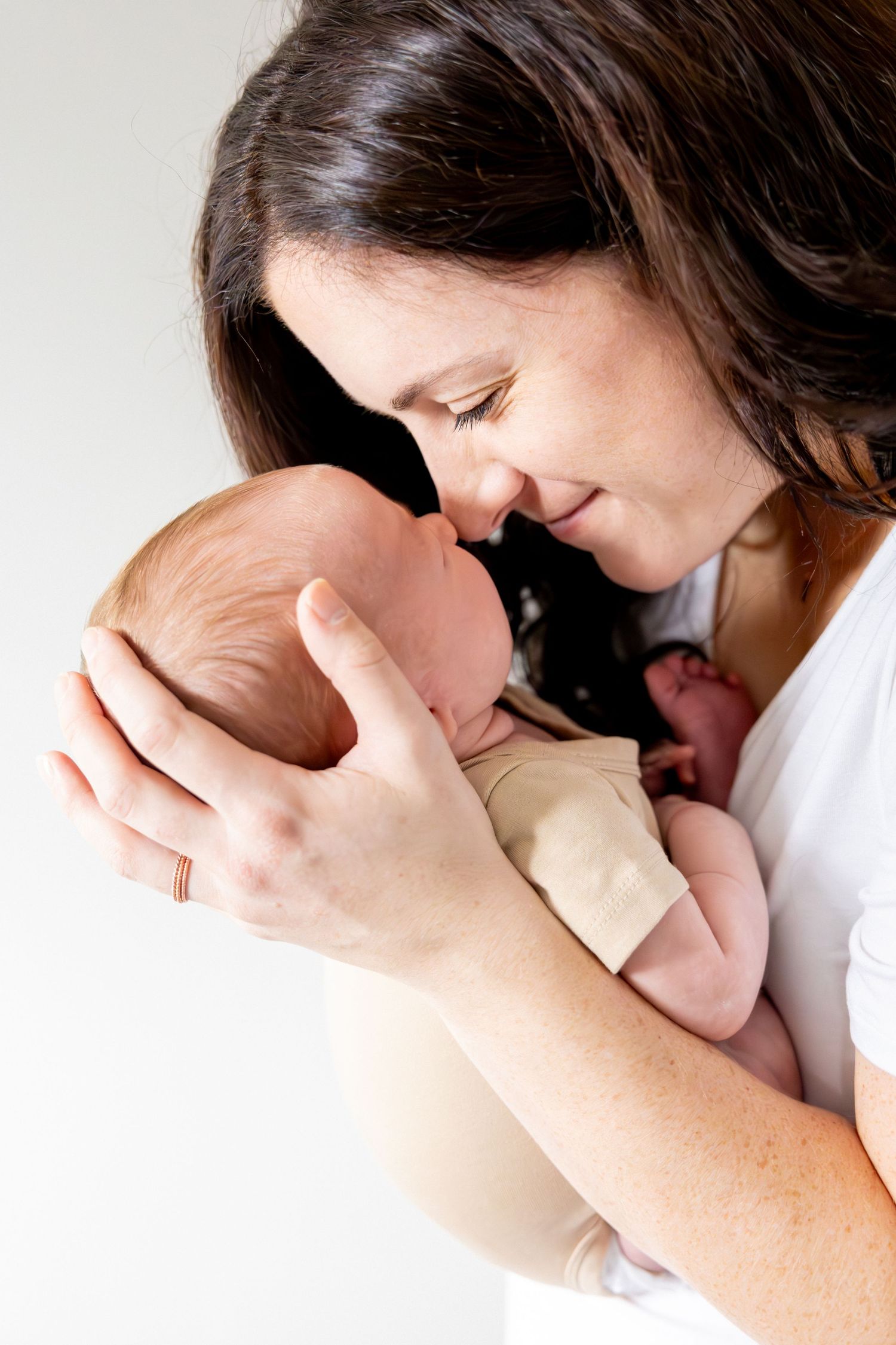 Intimate portrait of parent cradling and nuzzling newborn baby against white background.