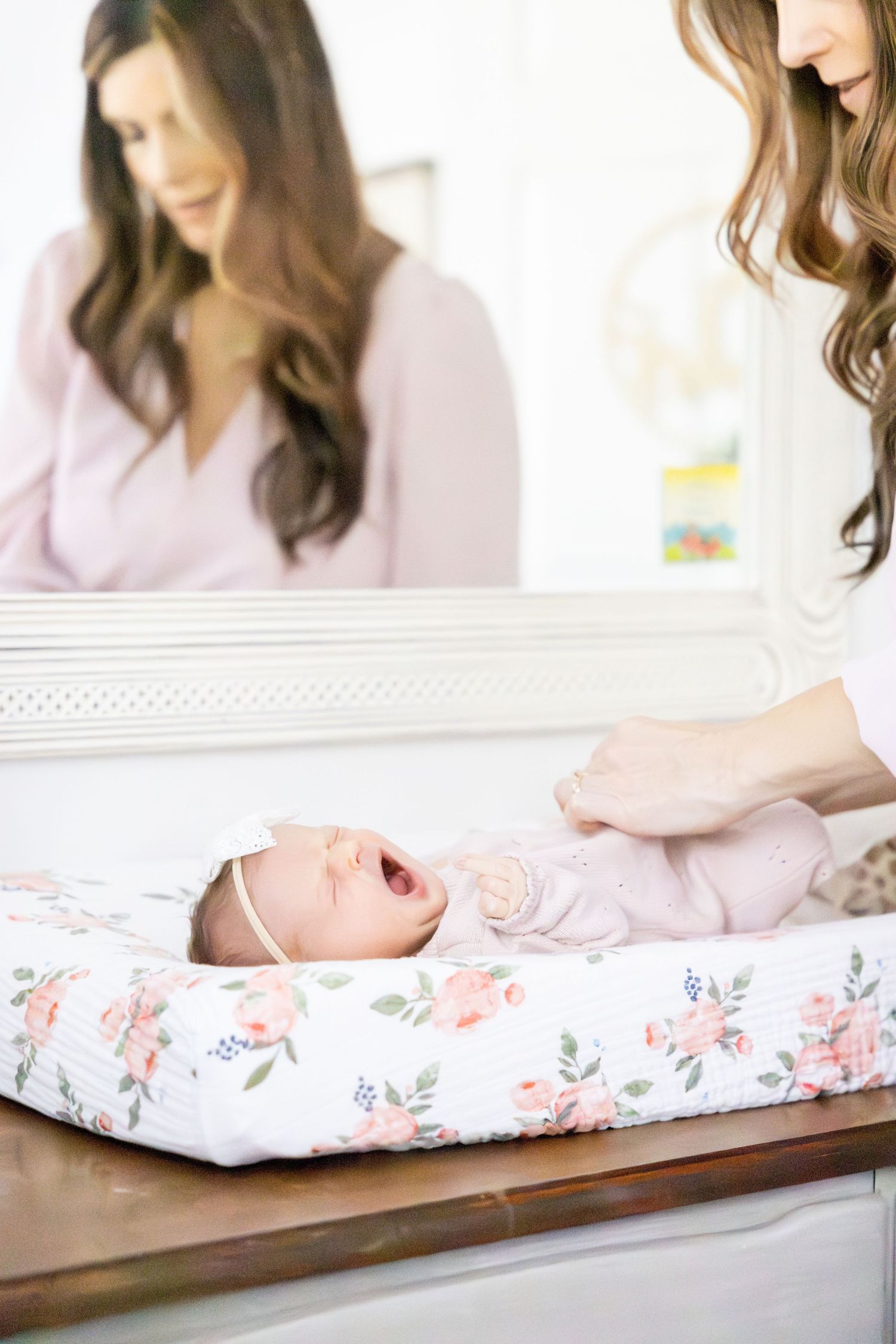 Floral changing pad on wooden surface with parent tending to baby in soft lighting.