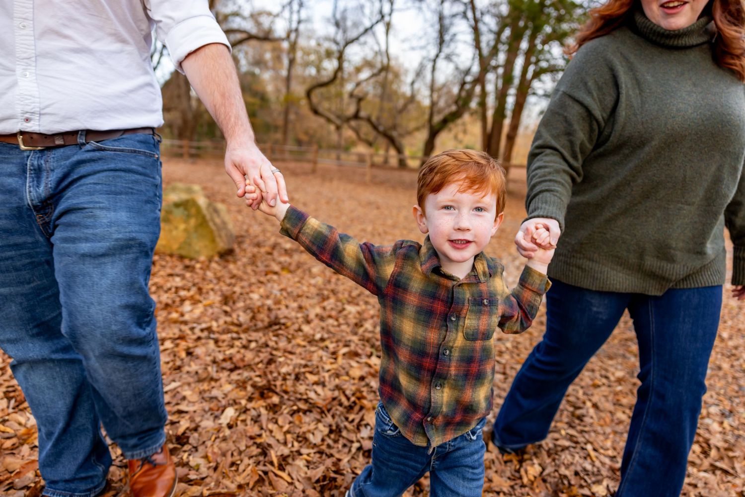 Family enjoying a playful moment together among fallen leaves during an autumn photo session.