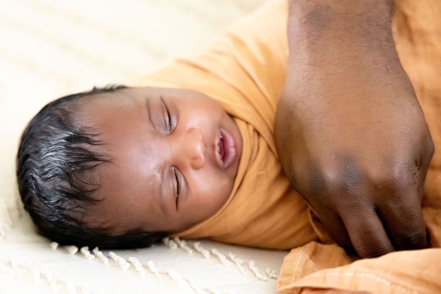 Sleeping baby in orange outfit lying on white blanket.