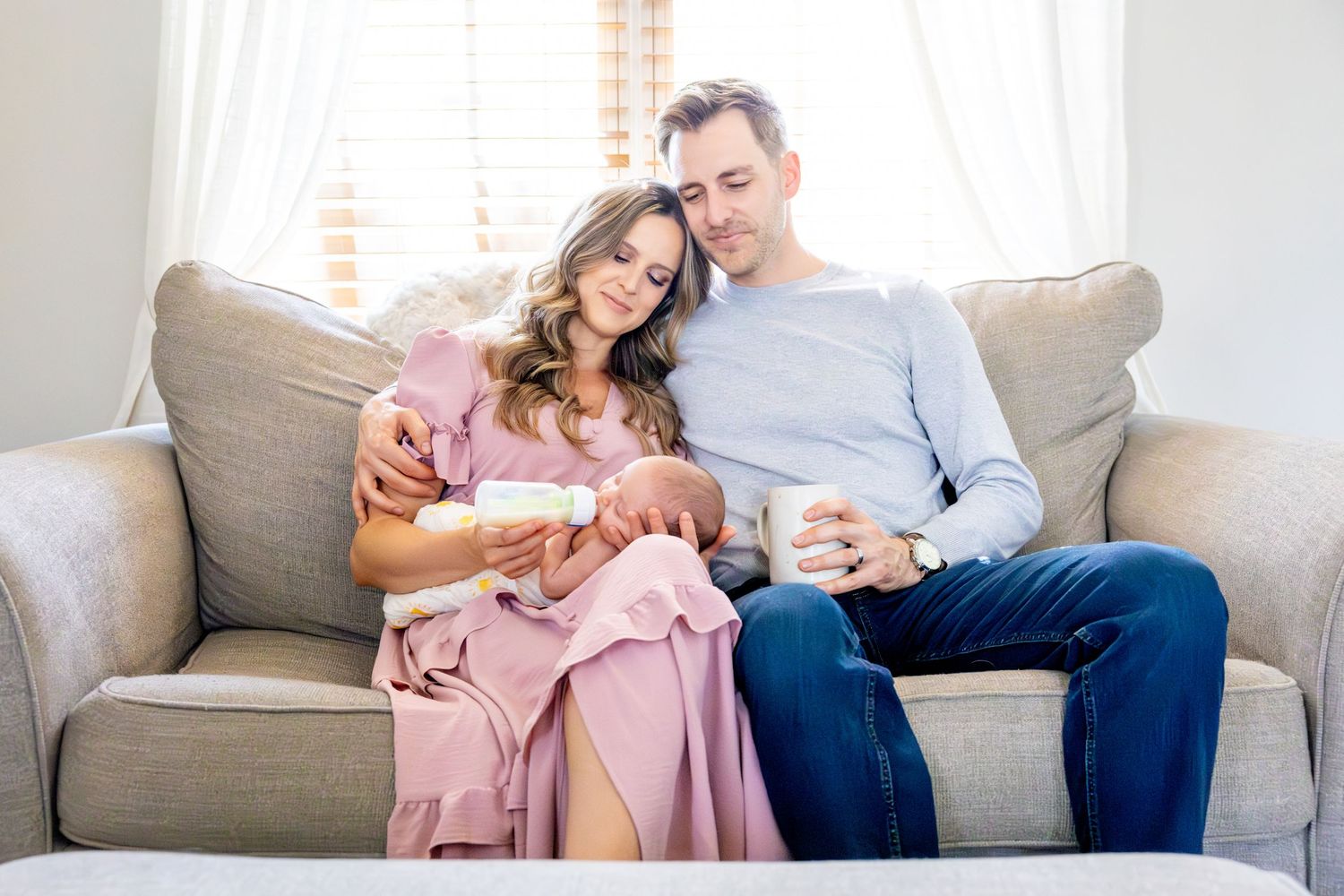 Couple sitting together on beige couch sharing intimate moment with newborn.