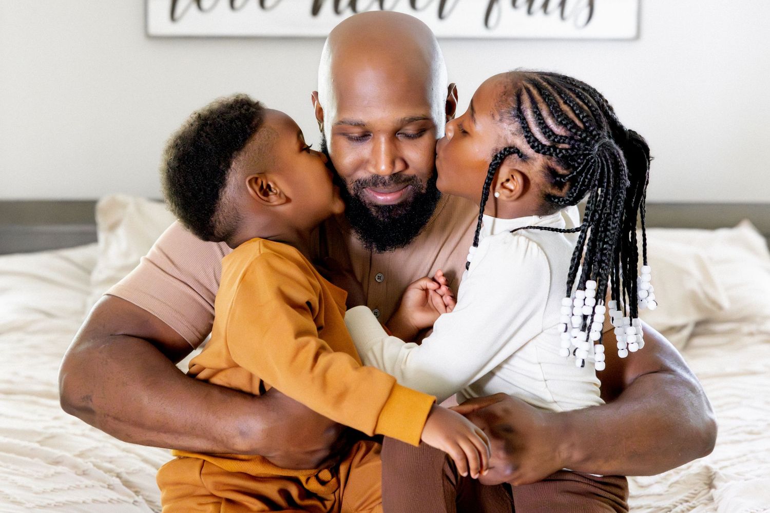Tender family moment captured on white bedding beneath wall art.