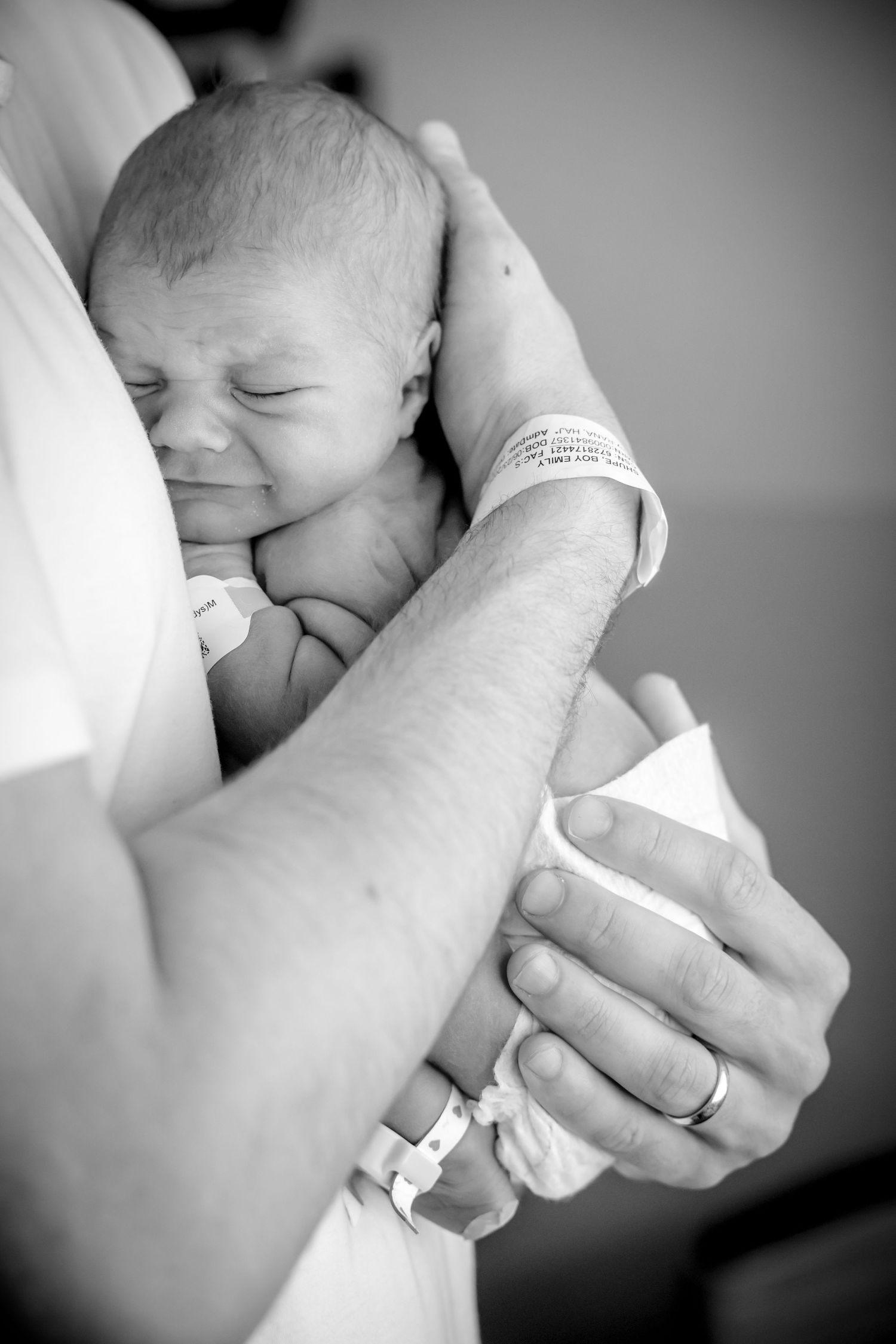 Black and white photo of newborn wearing hospital bracelet being cradled in arms.