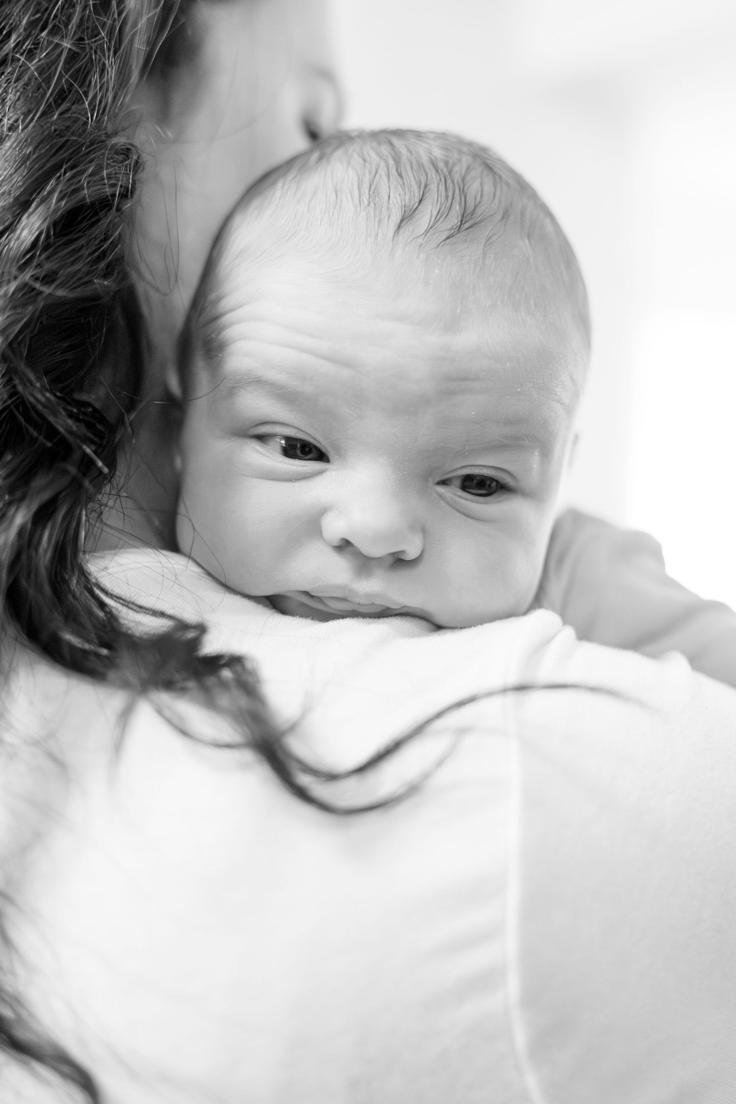 Close up black and white portrait of newborn baby being held against parent's shoulder.