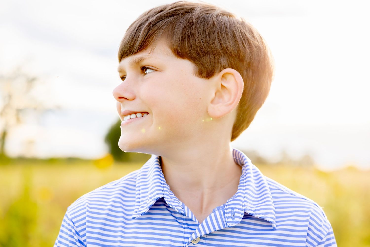 Close up portrait in sunshine wearing blue striped shirt against blurred meadow background at Blue Hill Garden in Monroe, NC.