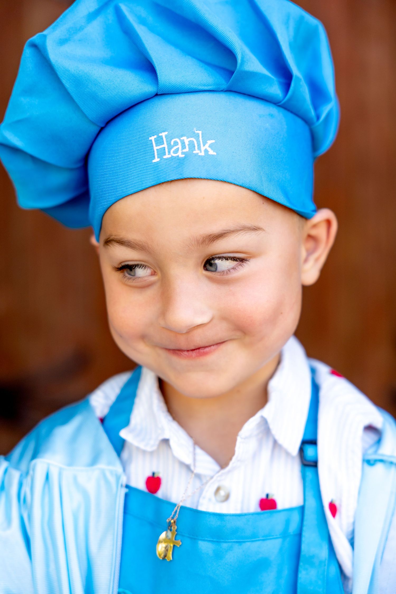 A small preschool graduate showing off his blue chef hat and apron.