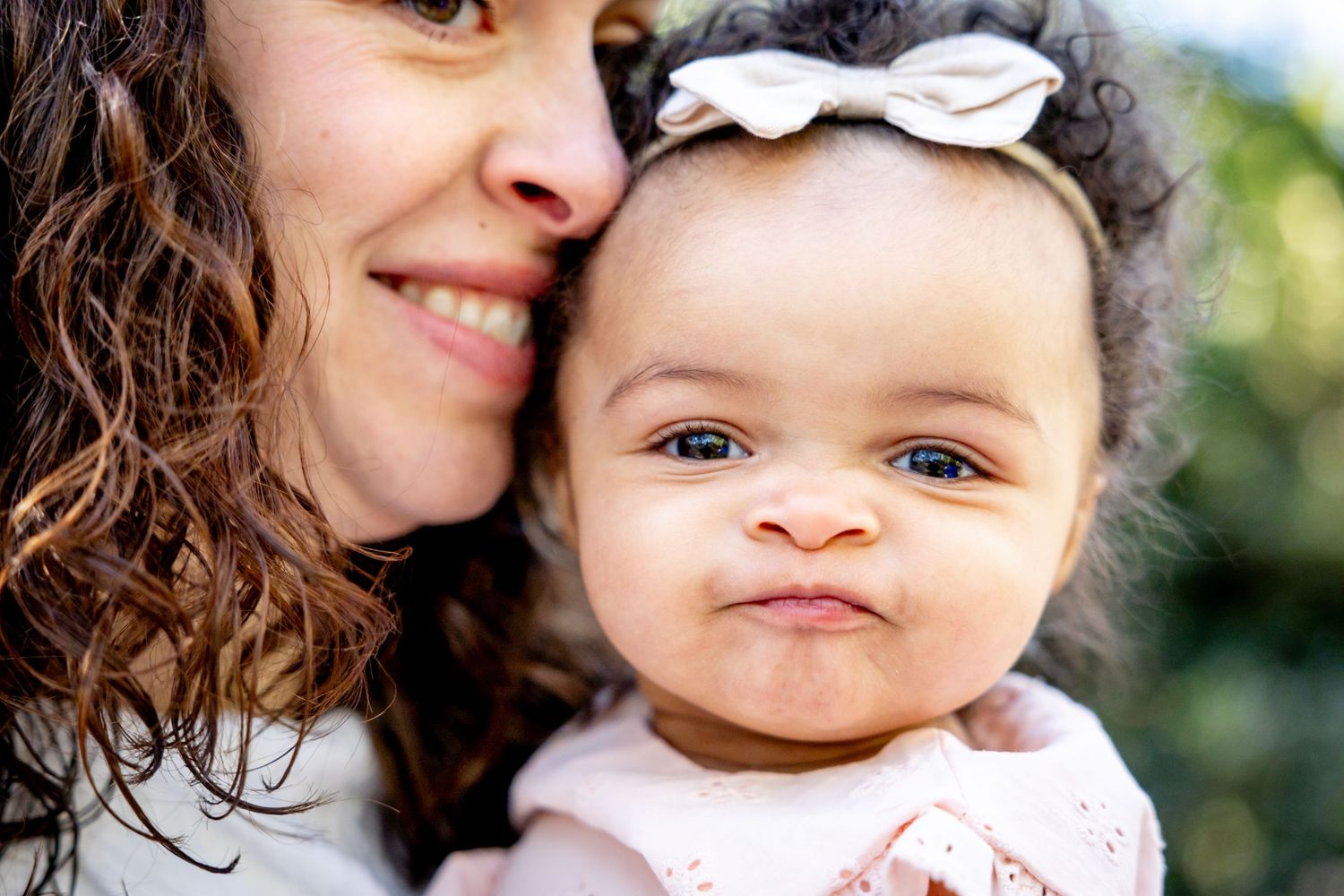 A tender close-up portrait showing joyful expressions and connection against blurred greenery.